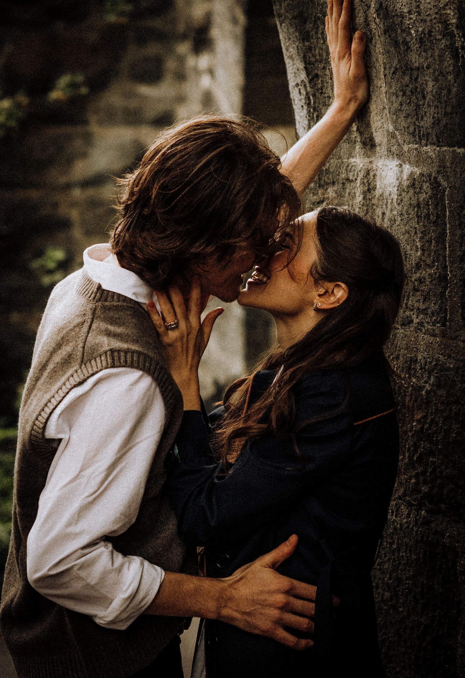 A romantic moment shared between two people against a tree in natural lighting.