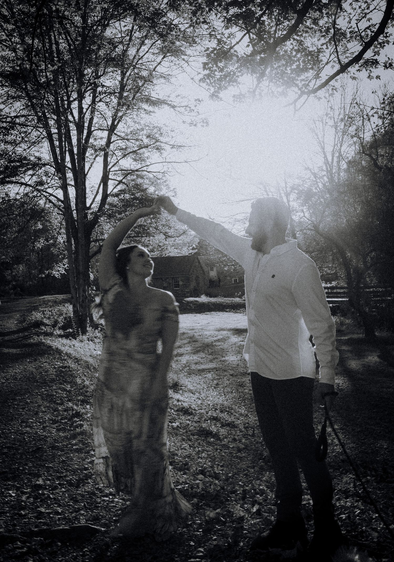 Atmospheric black and white photo of two figures standing in a misty wooded area near a rustic building.