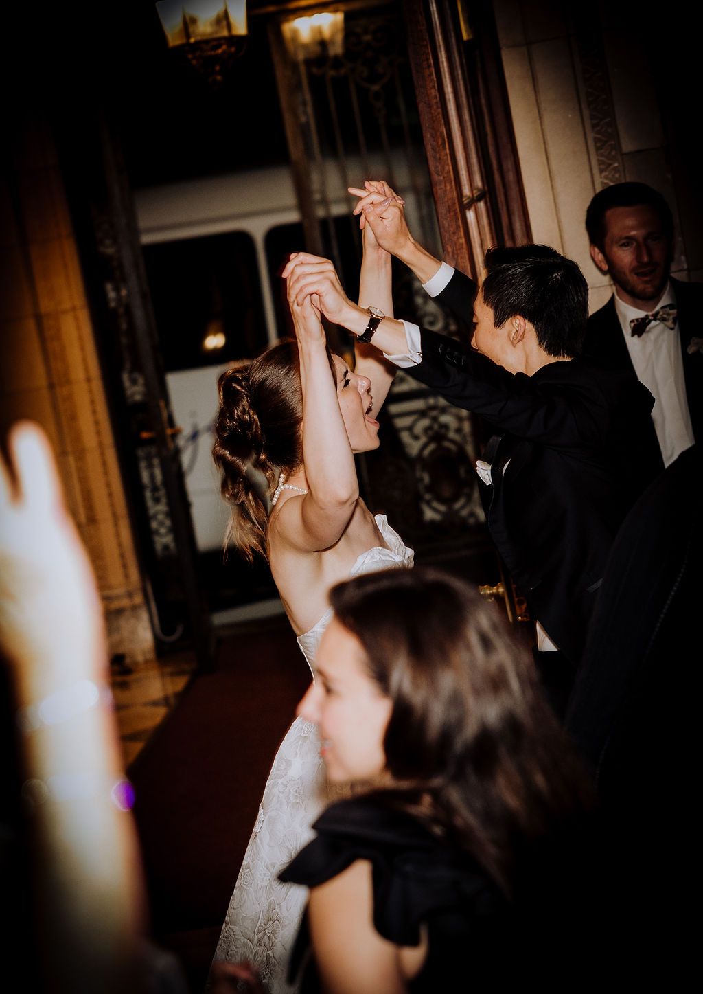 Bride and groom dancing joyfully with raised hands at elegant wedding reception venue.
