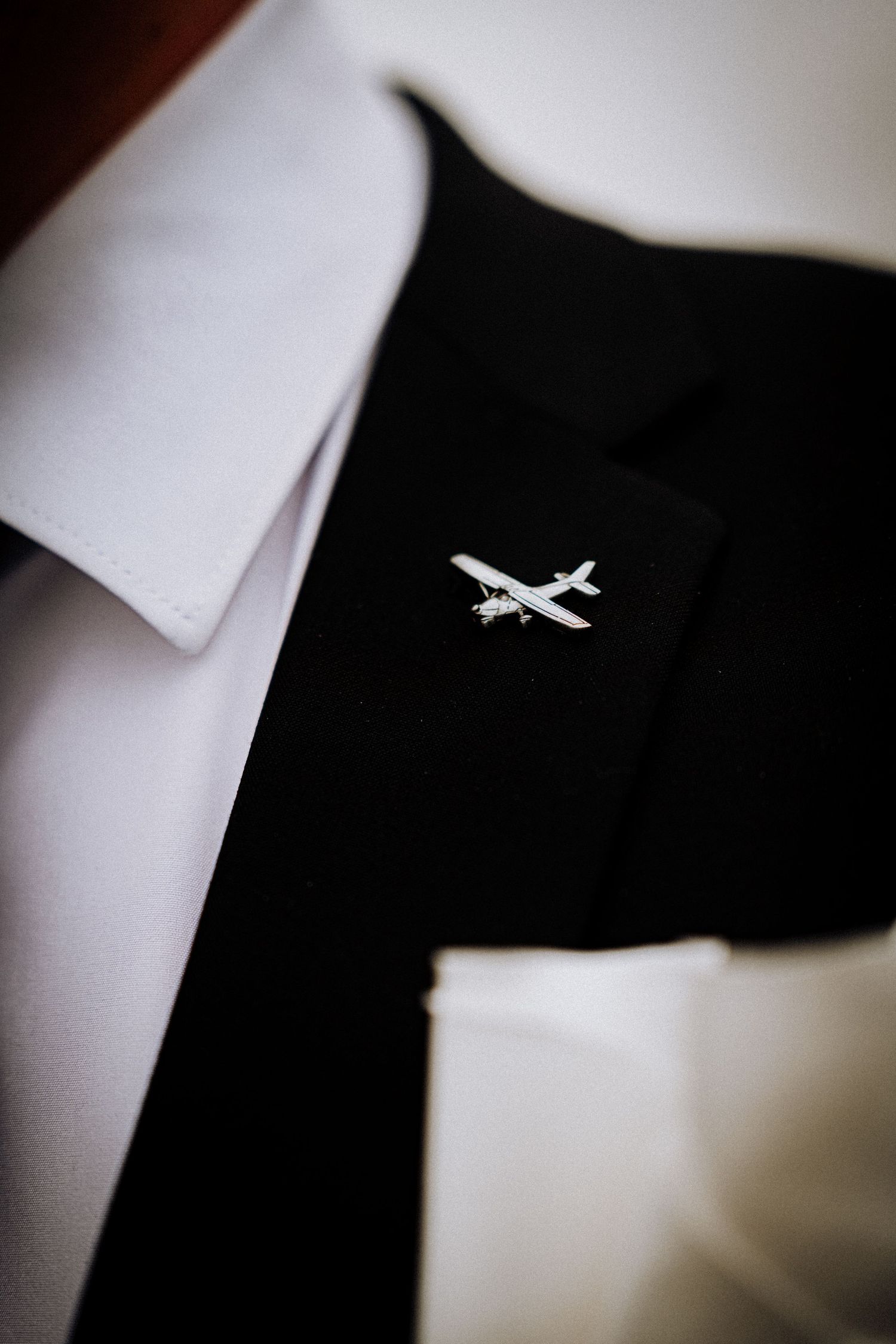Close-up detail of small airplane pin on black suit lapel.