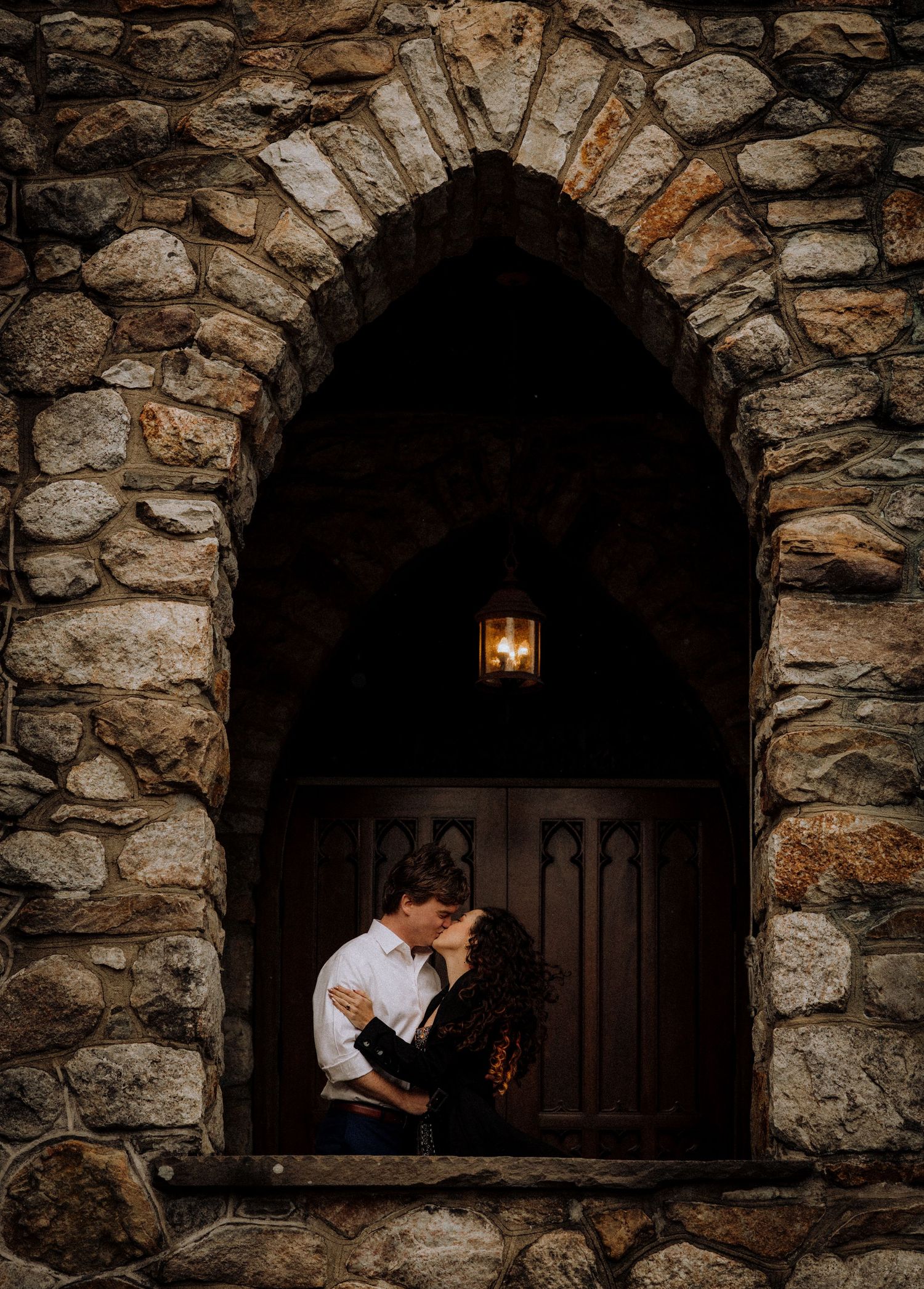 A romantic moment captured in a stone archway with dramatic lighting and shadows.