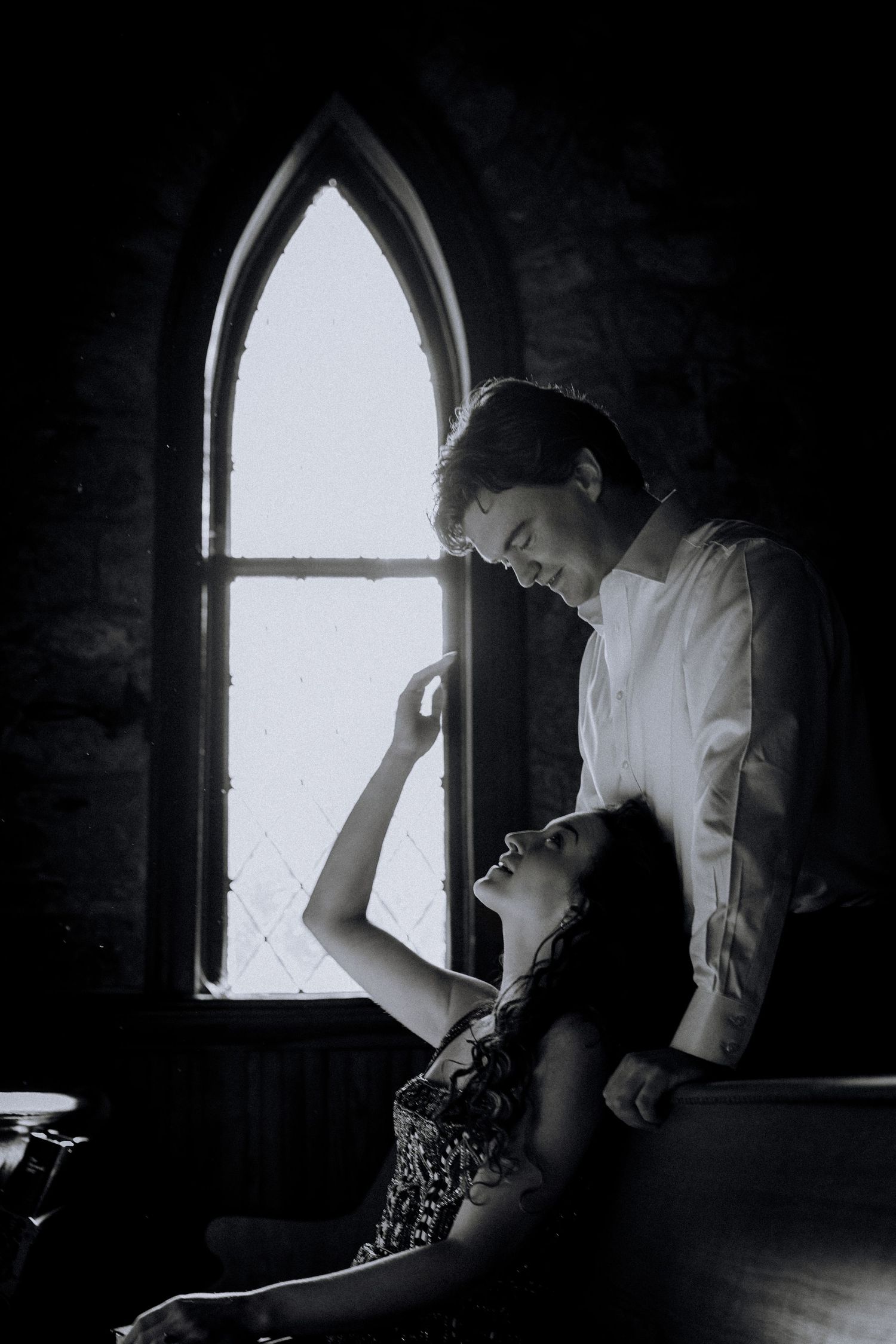 Moody silhouette against arched church window during intimate moment.