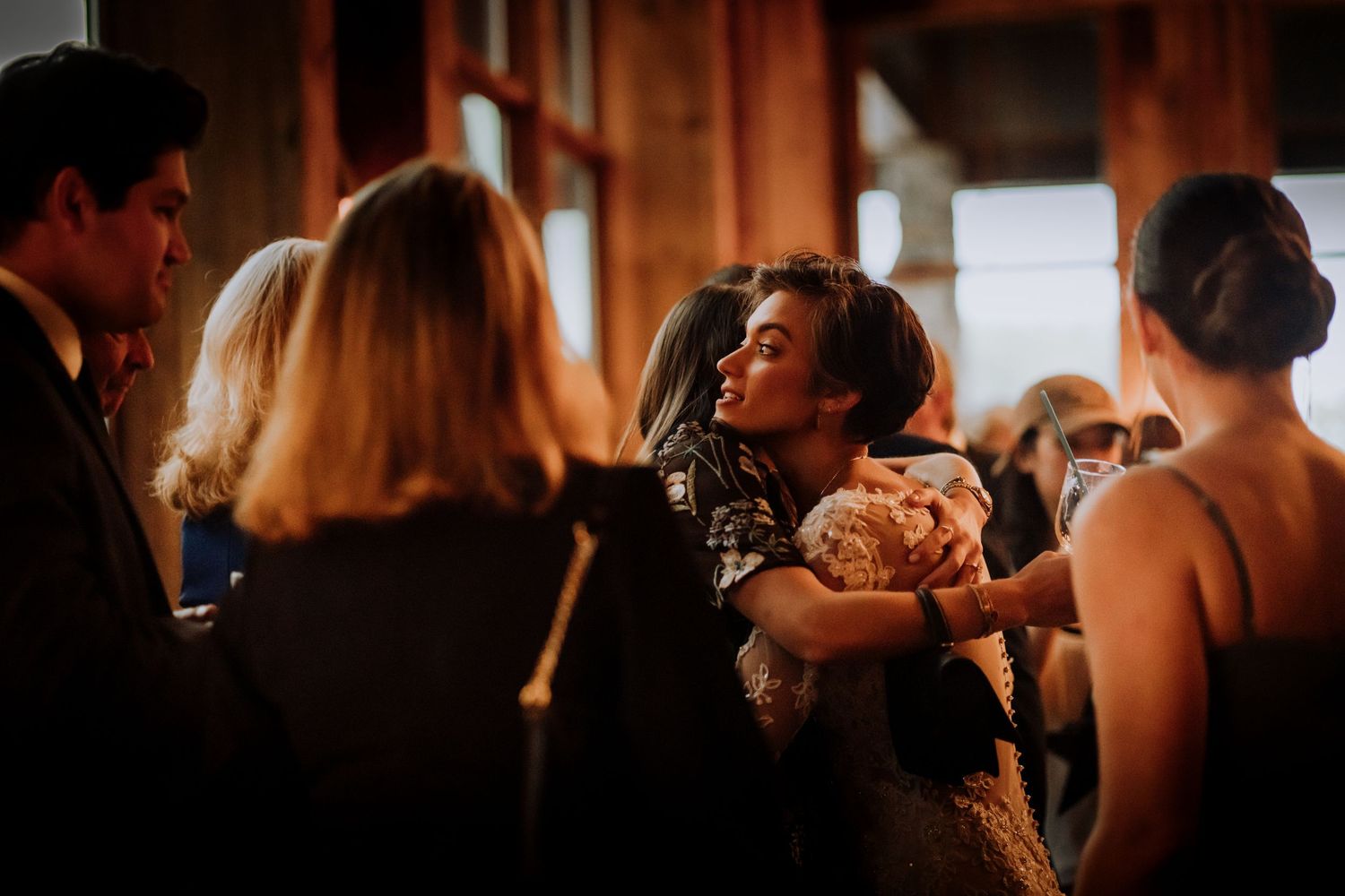 Wedding guests gather intimately in a warmly lit room during a reception celebration.