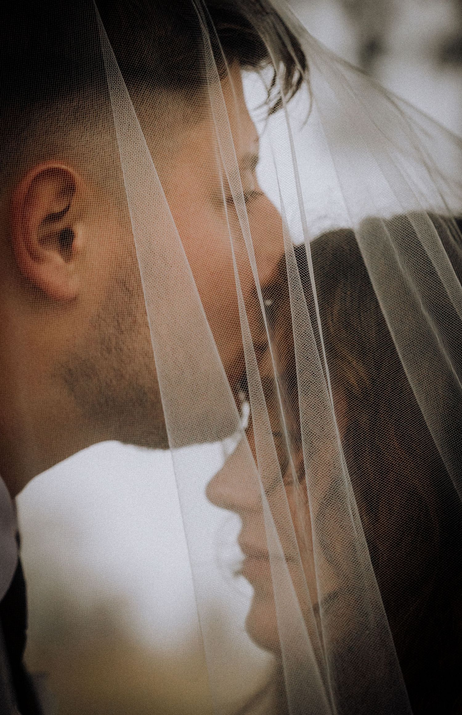 An artistic close-up wedding portrait through delicate white veil fabric.