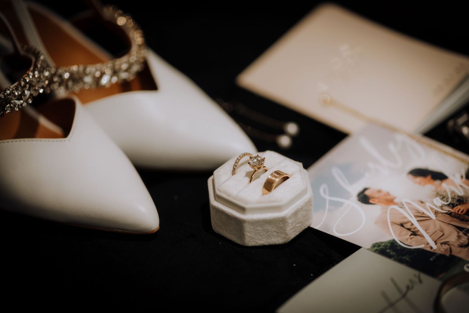 Wedding detail shot of rings and decorative elements on white surface.