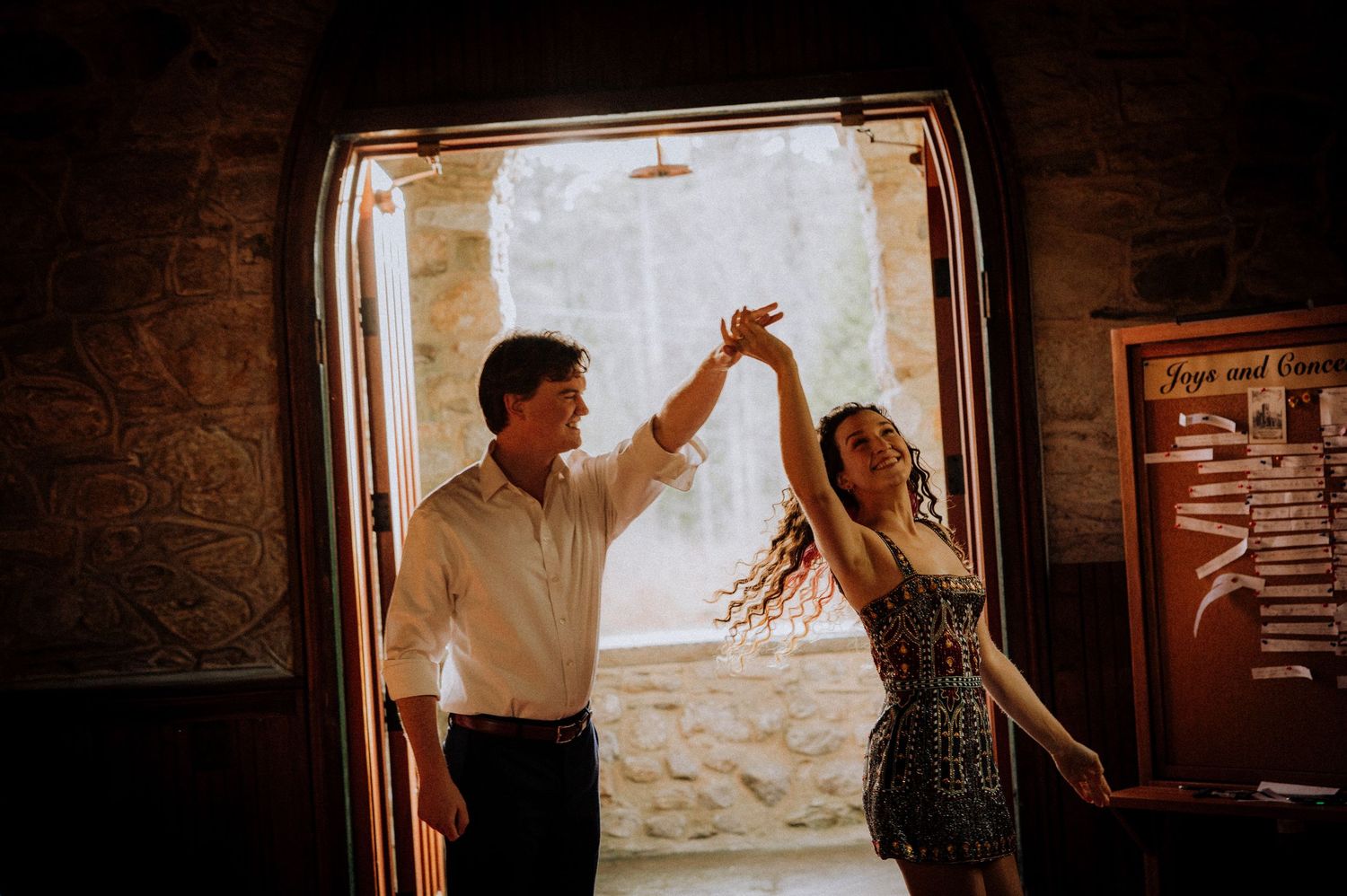 Couple dancing in sunlit doorway of historic stone building.