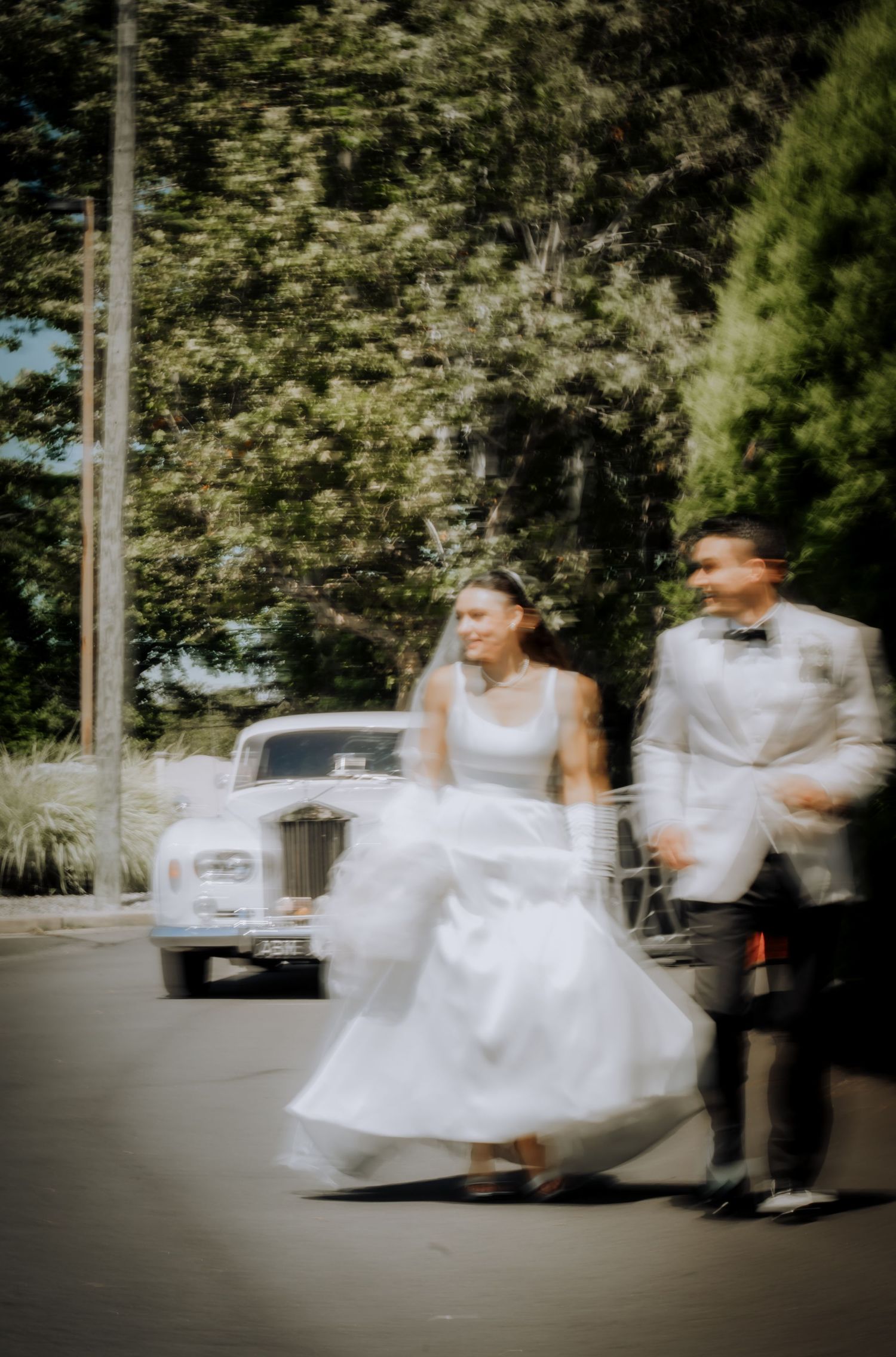 A vintage-style wedding photo of a couple walking together near a classic car.