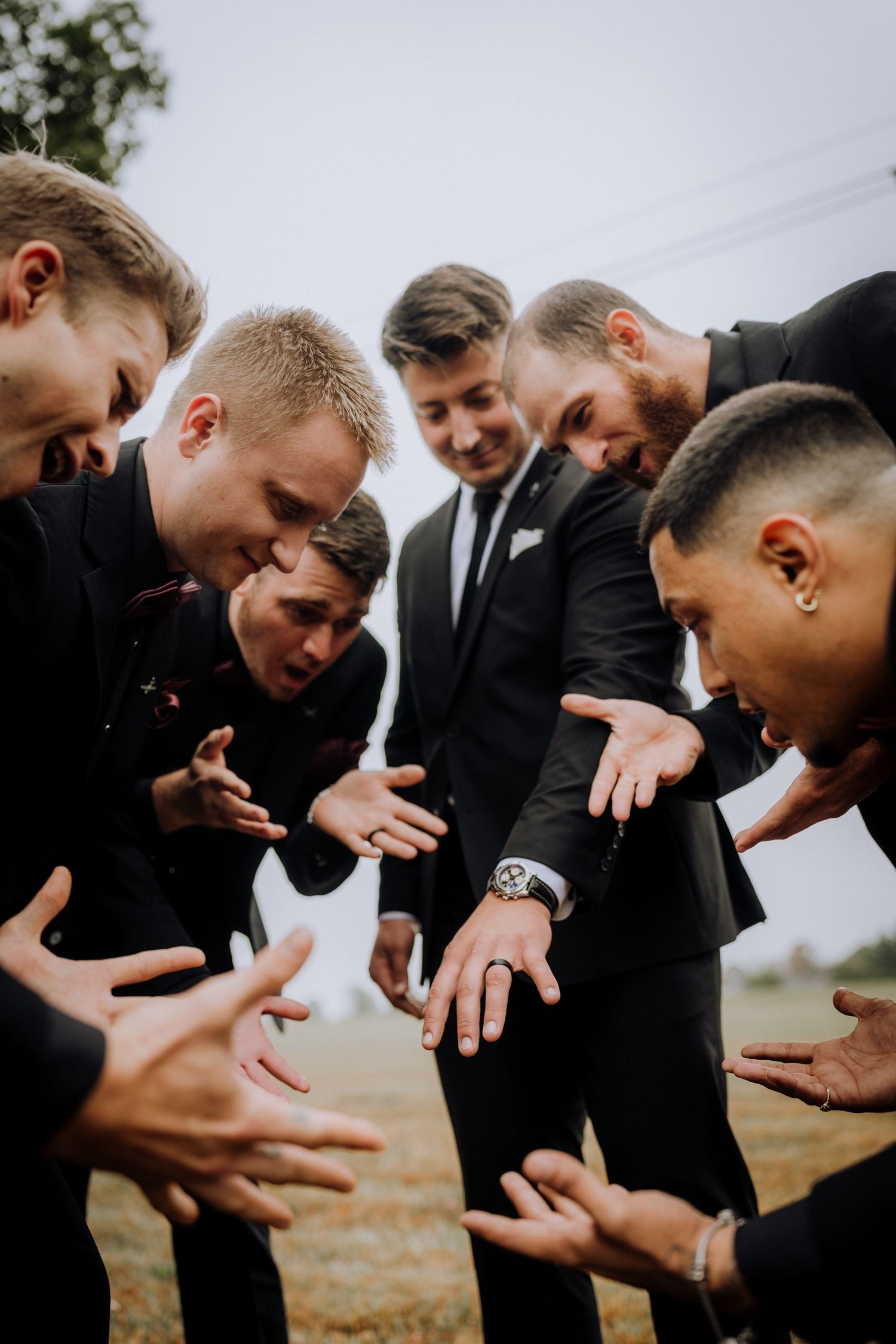 Groomsmen in black suits huddle together looking at their hands.