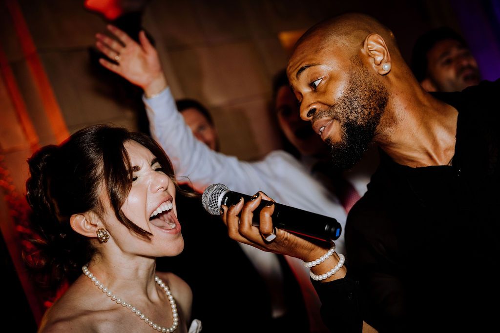 Bride and groom singing into microphone together at wedding reception party celebration.