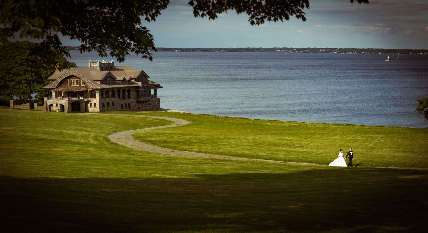 Bride and groom share a romantic moment on a lush green lawn overlooking a serene waterfront estate.
