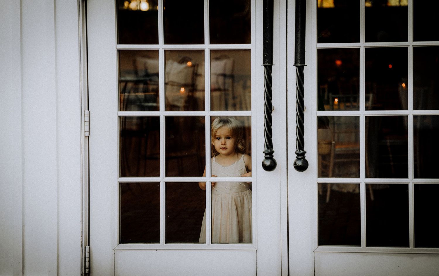 A vintage-style photo of a figure looking through white French doors.