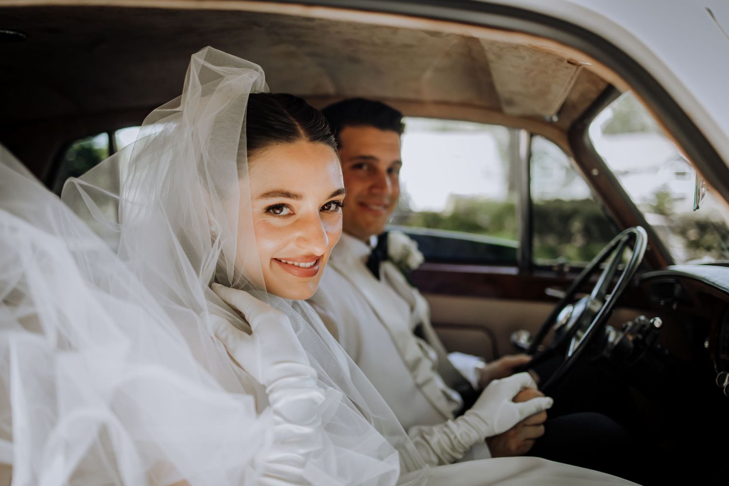 Classic car wedding scene with flowing white veil in natural light.
