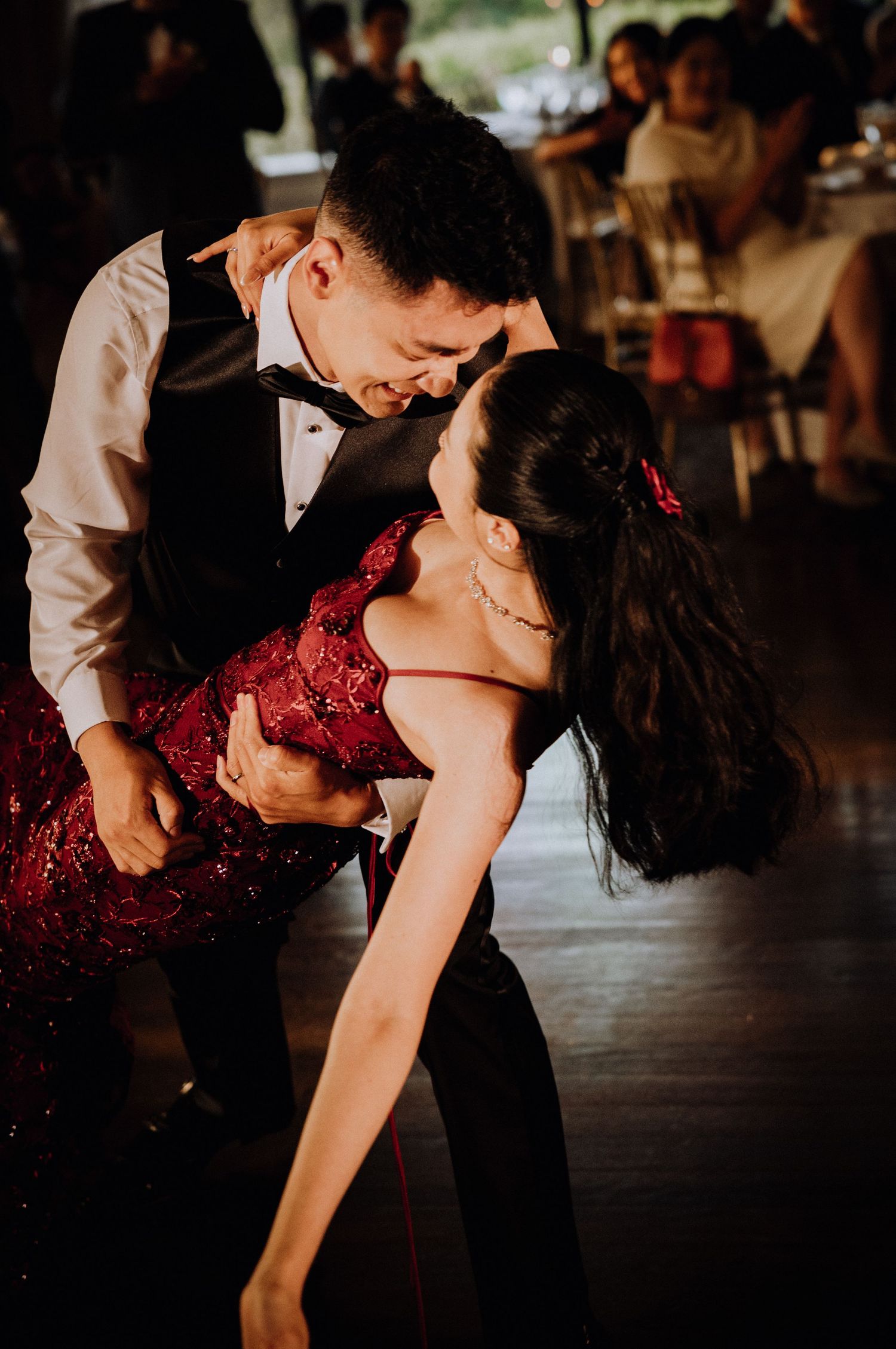 Couple sharing an intimate dance, man in tuxedo vest dipping woman in red sequin dress at a wedding reception.