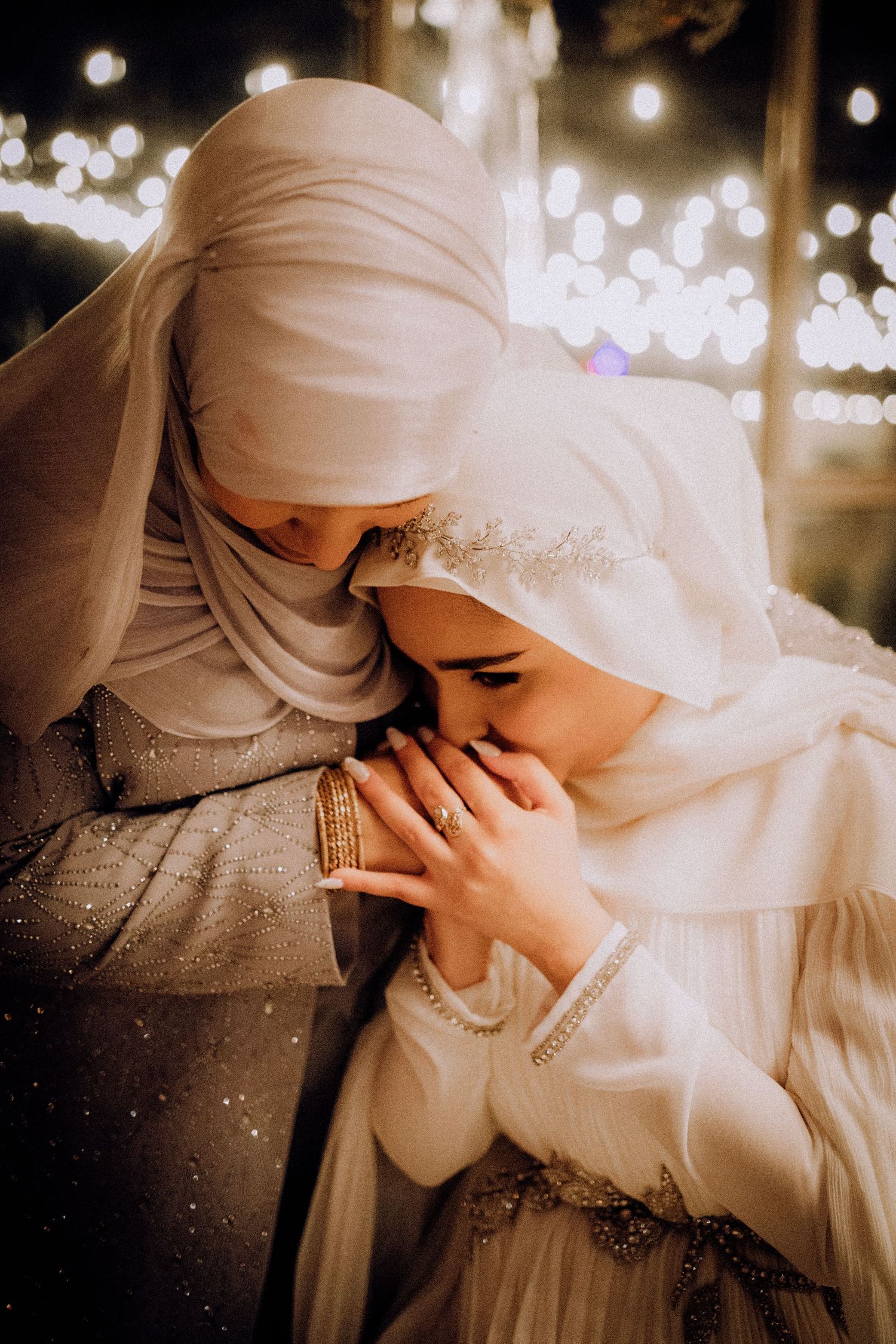 Tender moments between couple in traditional white wedding attire captured under string lights.