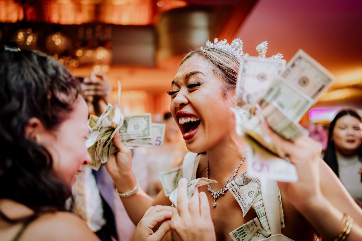 Wedding guests celebrate with dollar bills in a festive party atmosphere with warm lighting.