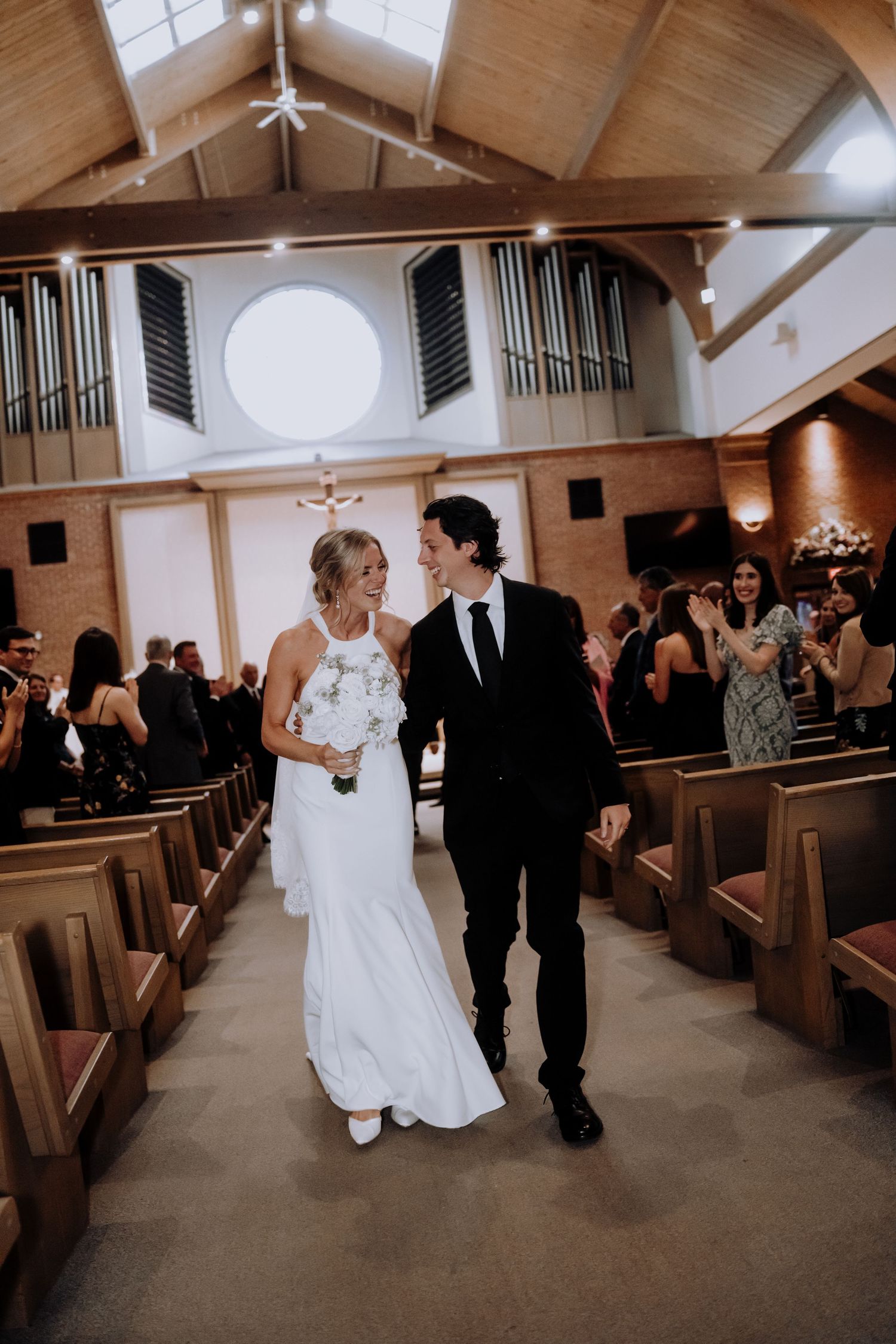 A couple walks down the church aisle between wooden pews.Editorial and Cinematic Wedding photos