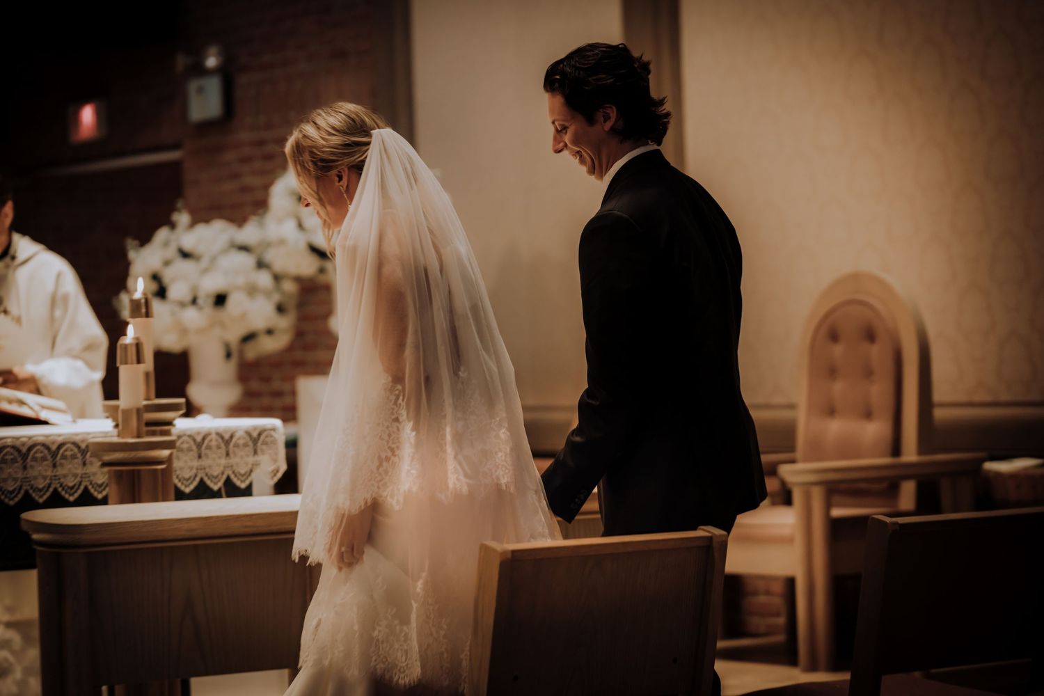 Wedding couple stands in warm-lit church sanctuary during intimate ceremony.