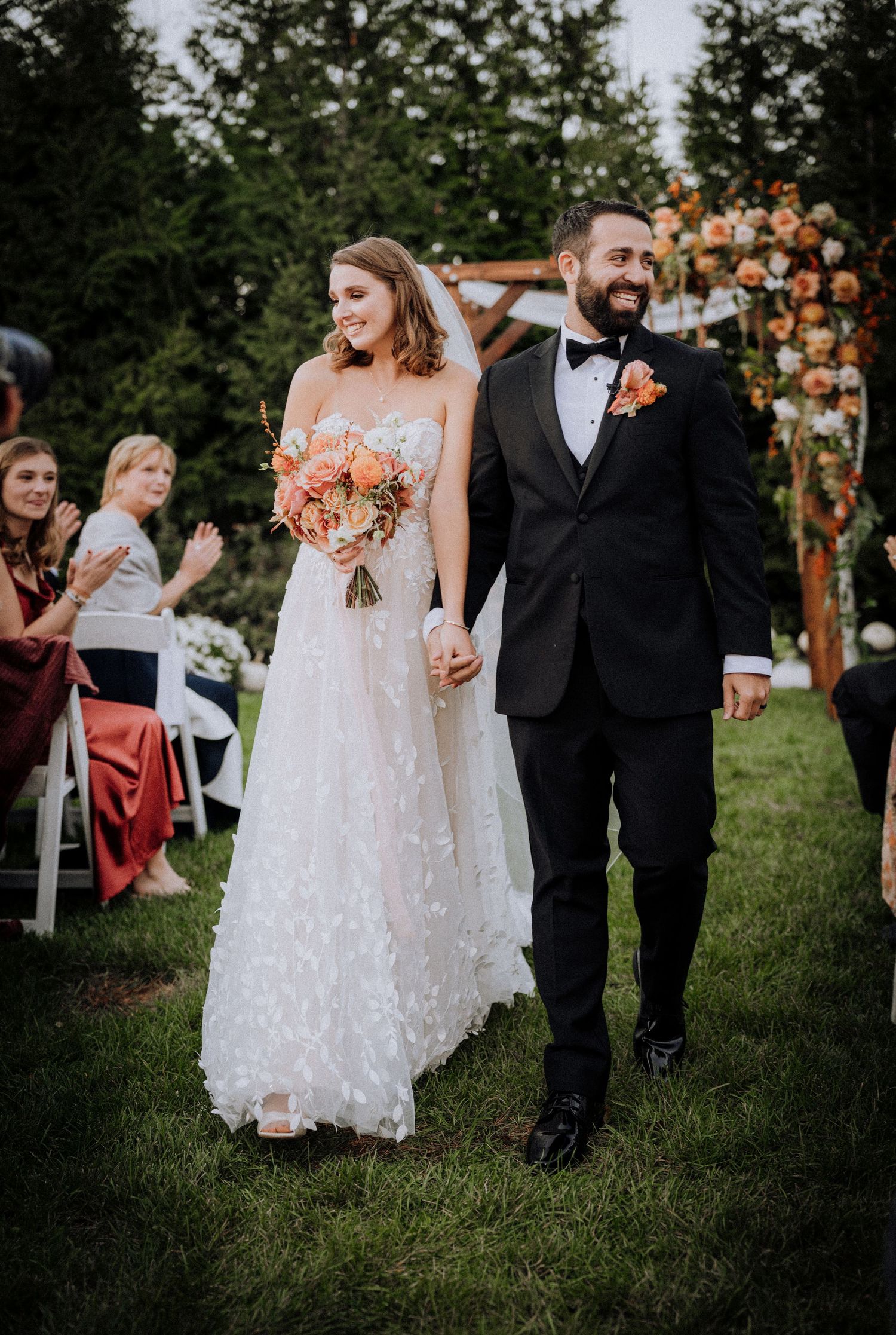 Wedding party walking through garden with floral arch and outdoor seating.