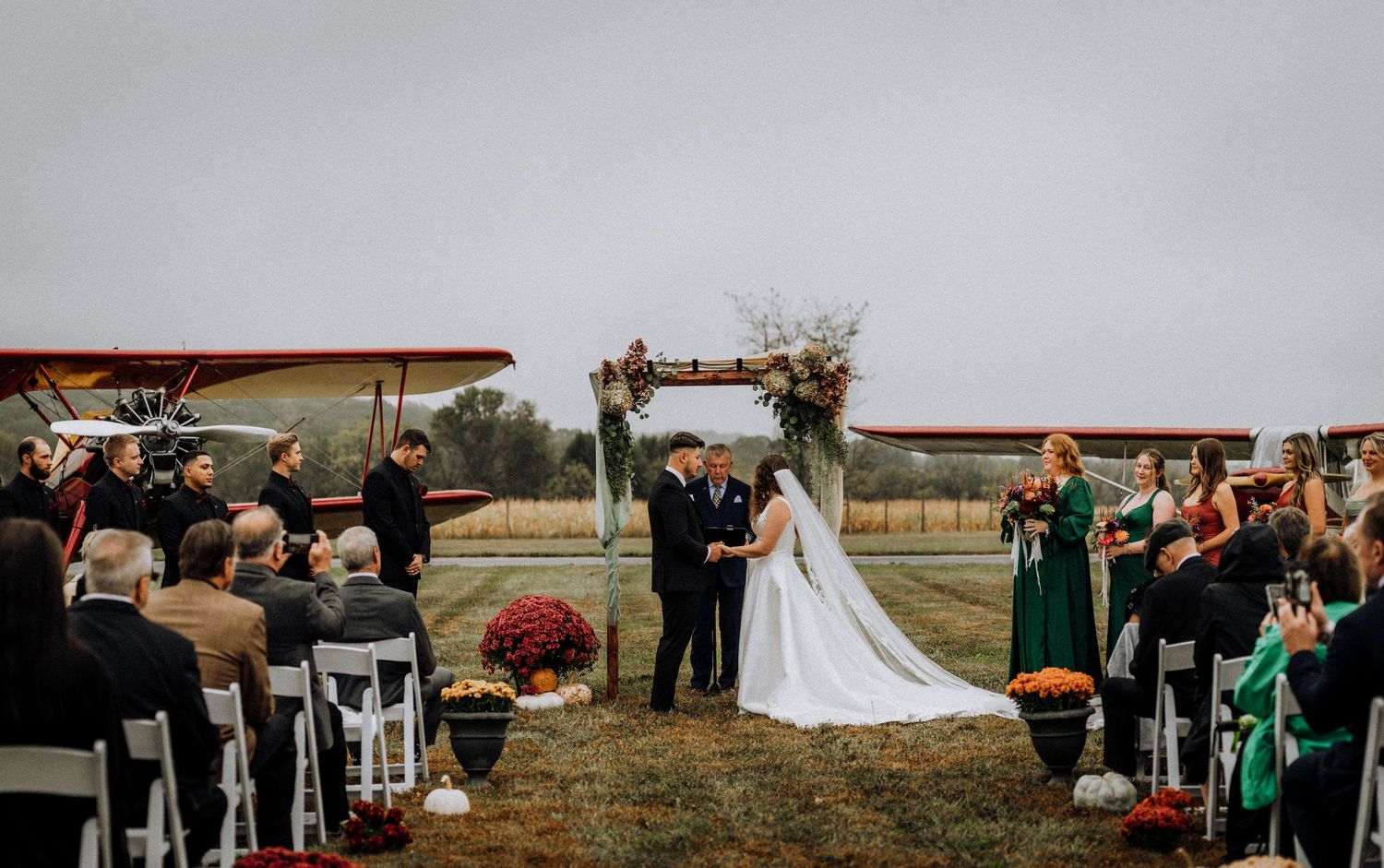 Outdoor wedding ceremony setup with vintage airplanes and emerald green decor.