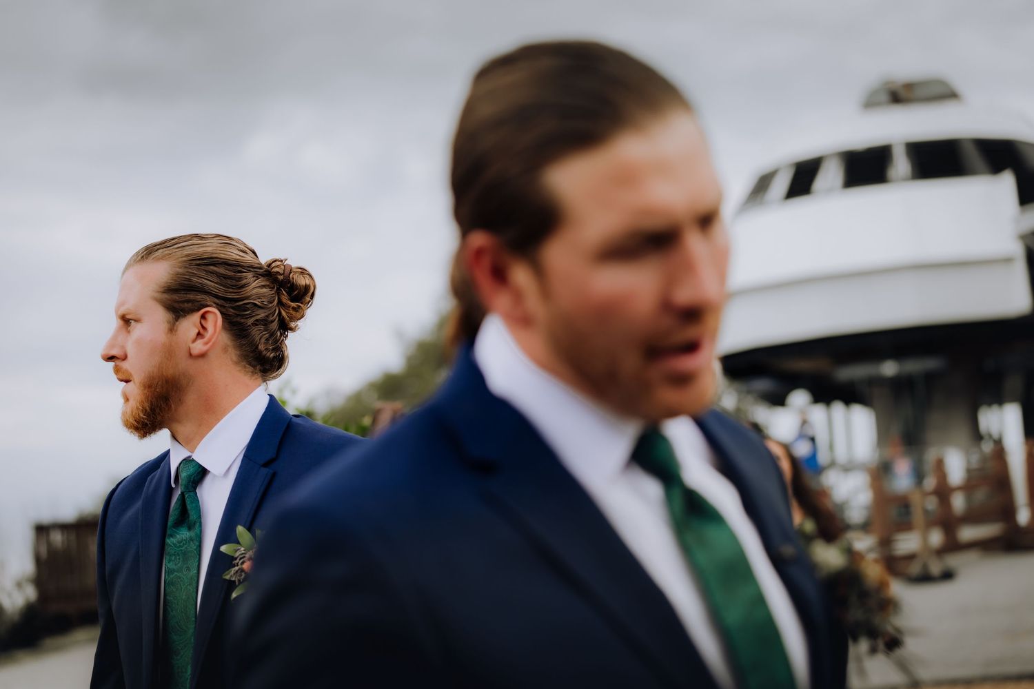 Groomsmen in navy suits with green ties walking together outdoors.