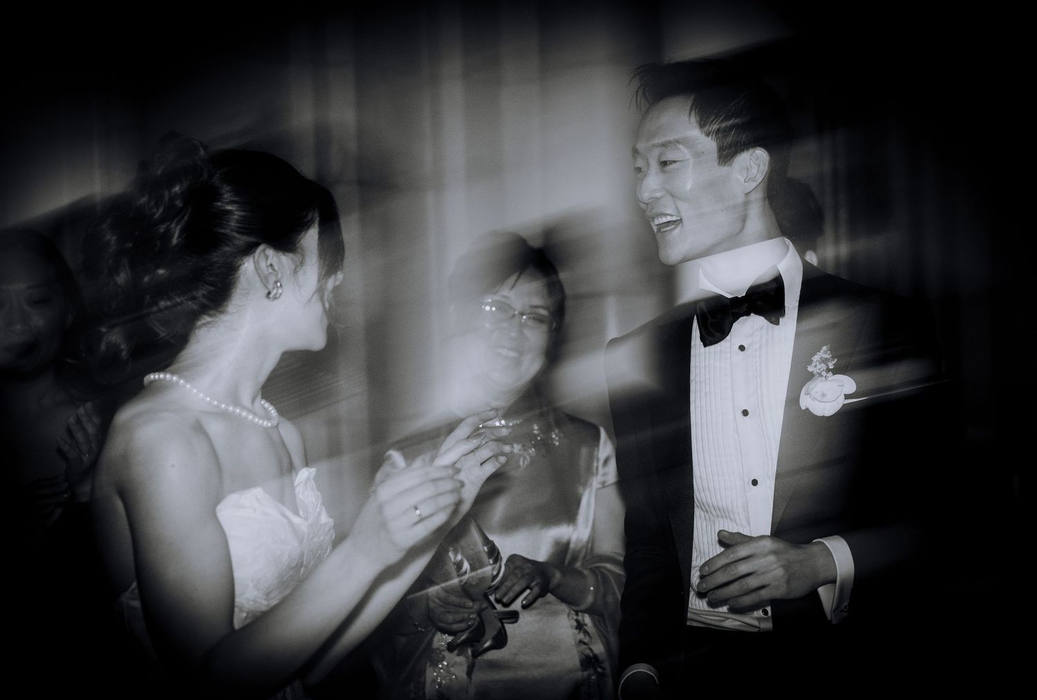 Black and white wedding photo of a smiling bride and groom exchanging rings with an officiant.