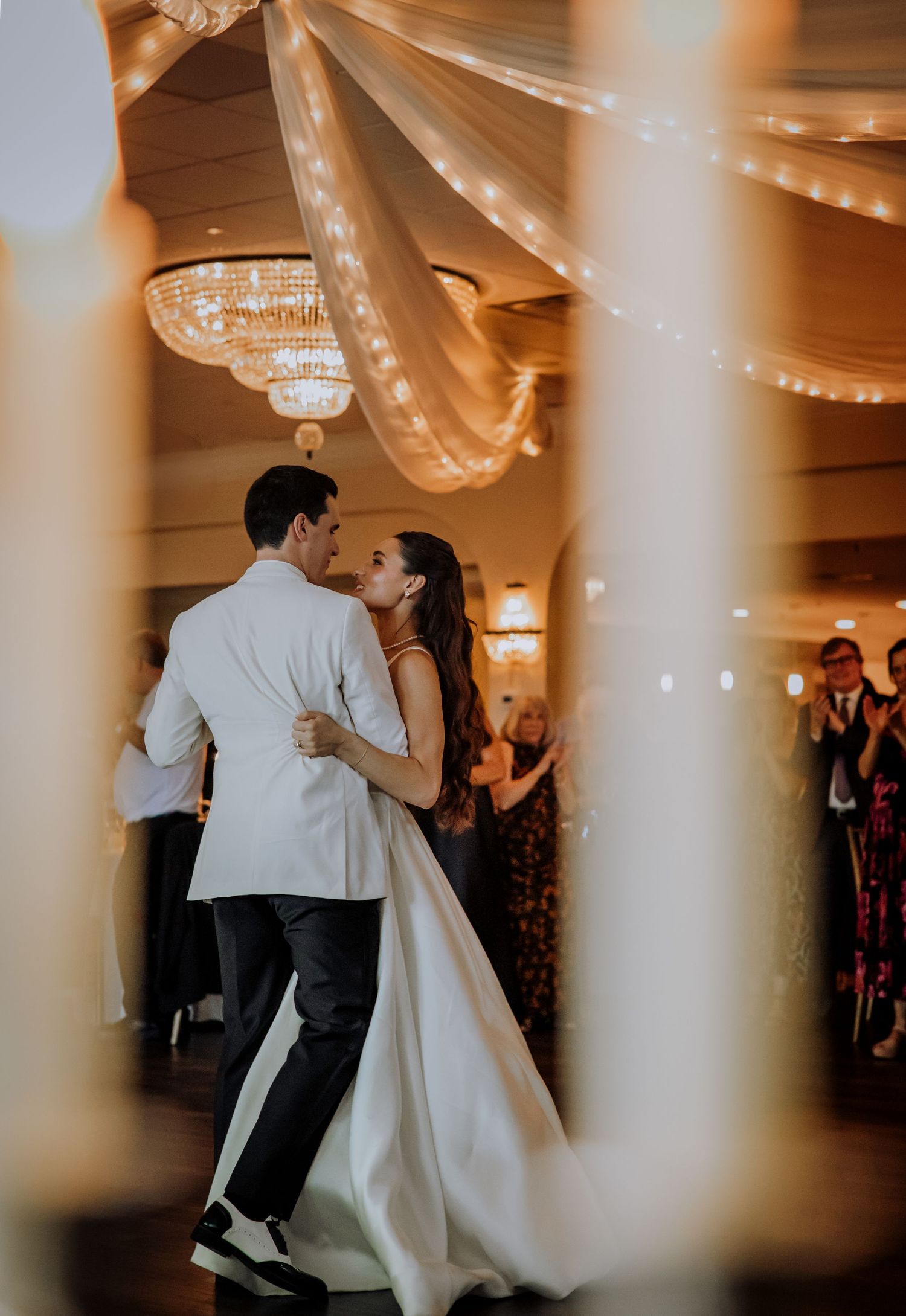 Couple dancing in an elegant ballroom with white draping and columns.