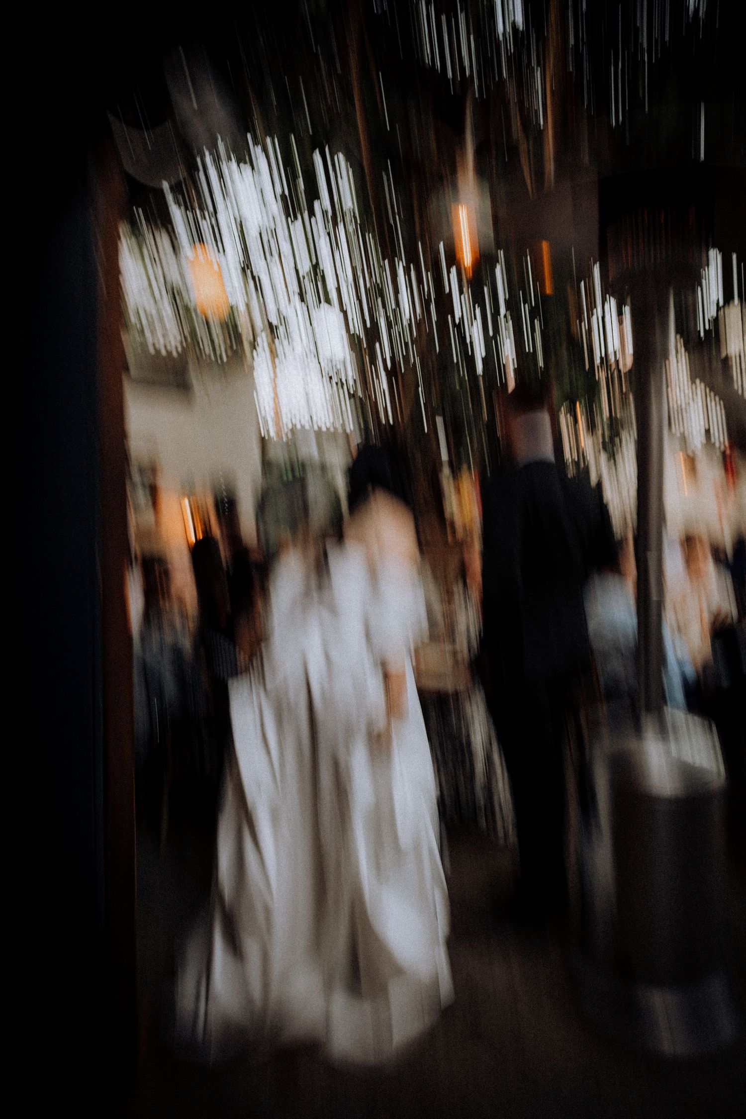 Blurred motion photo of a bride in white dress at an indoor wedding reception with bokeh lights.