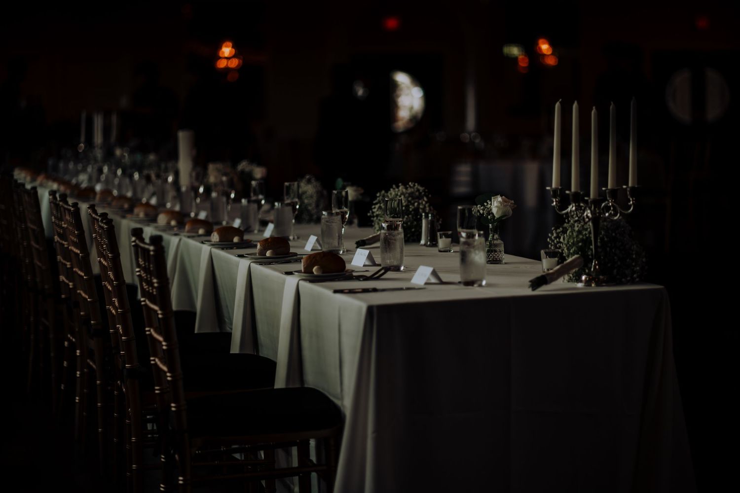 Dark reception hall set with elegant white tablecloths and place settings.