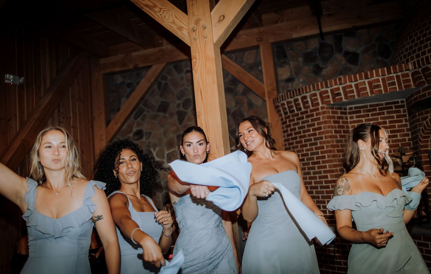 Bridesmaids in light blue dresses celebrating in rustic wooden venue.Editorial and Cinematic Wedding photos