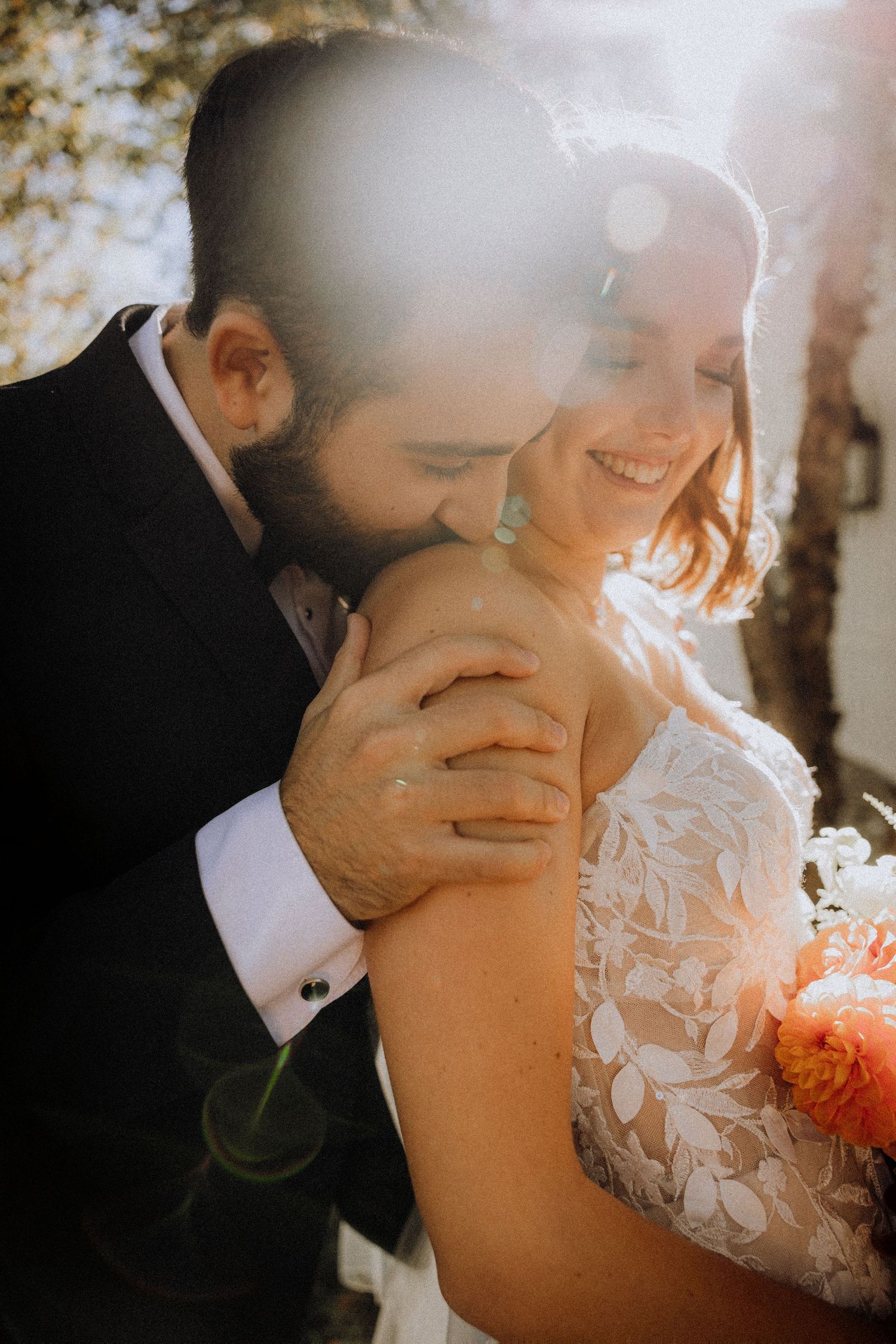 Intimate wedding couple moment captured in warm sunlight with delicate lace dress details.