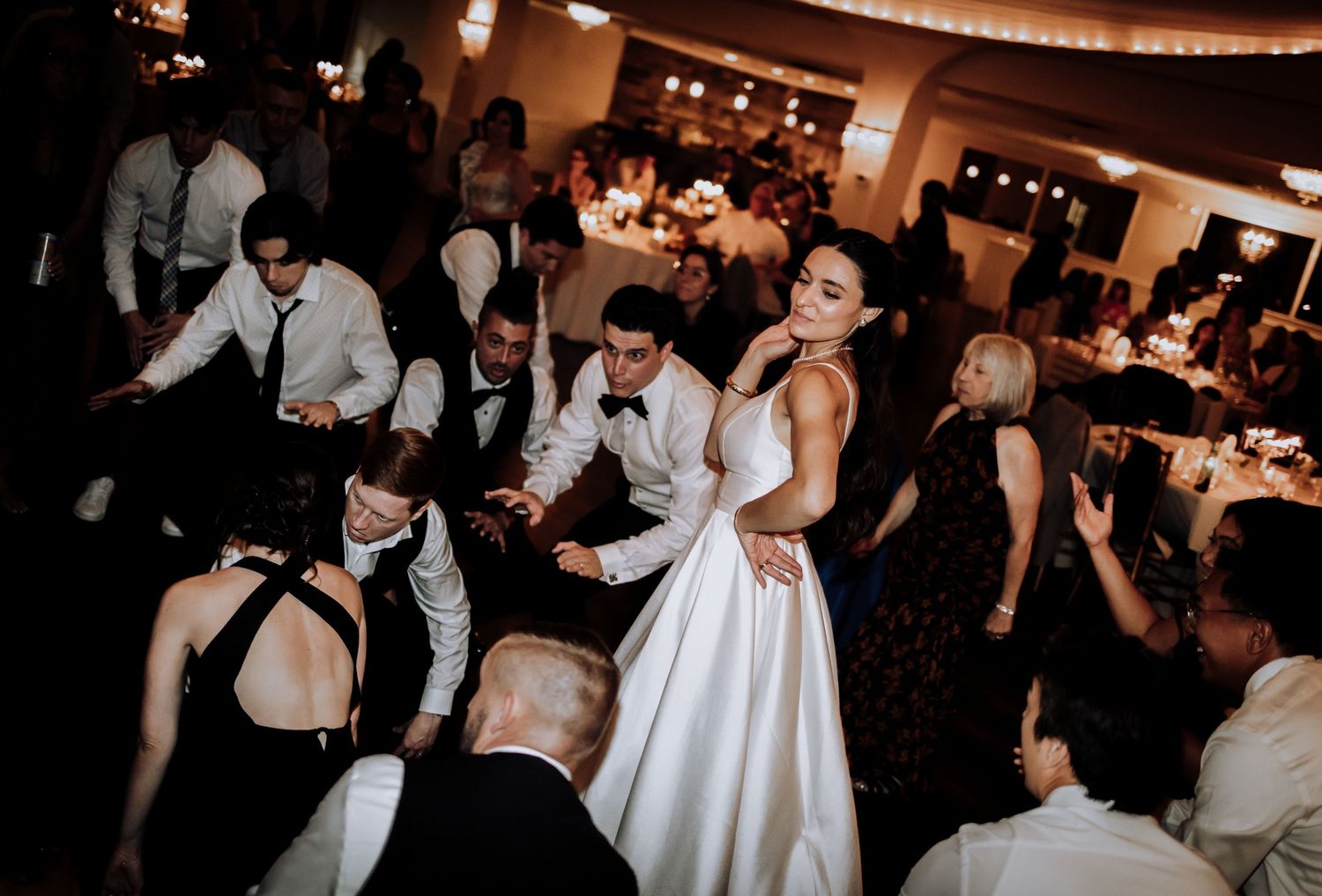 Wedding reception dance floor filled with guests celebrating around the bride in her white gown.