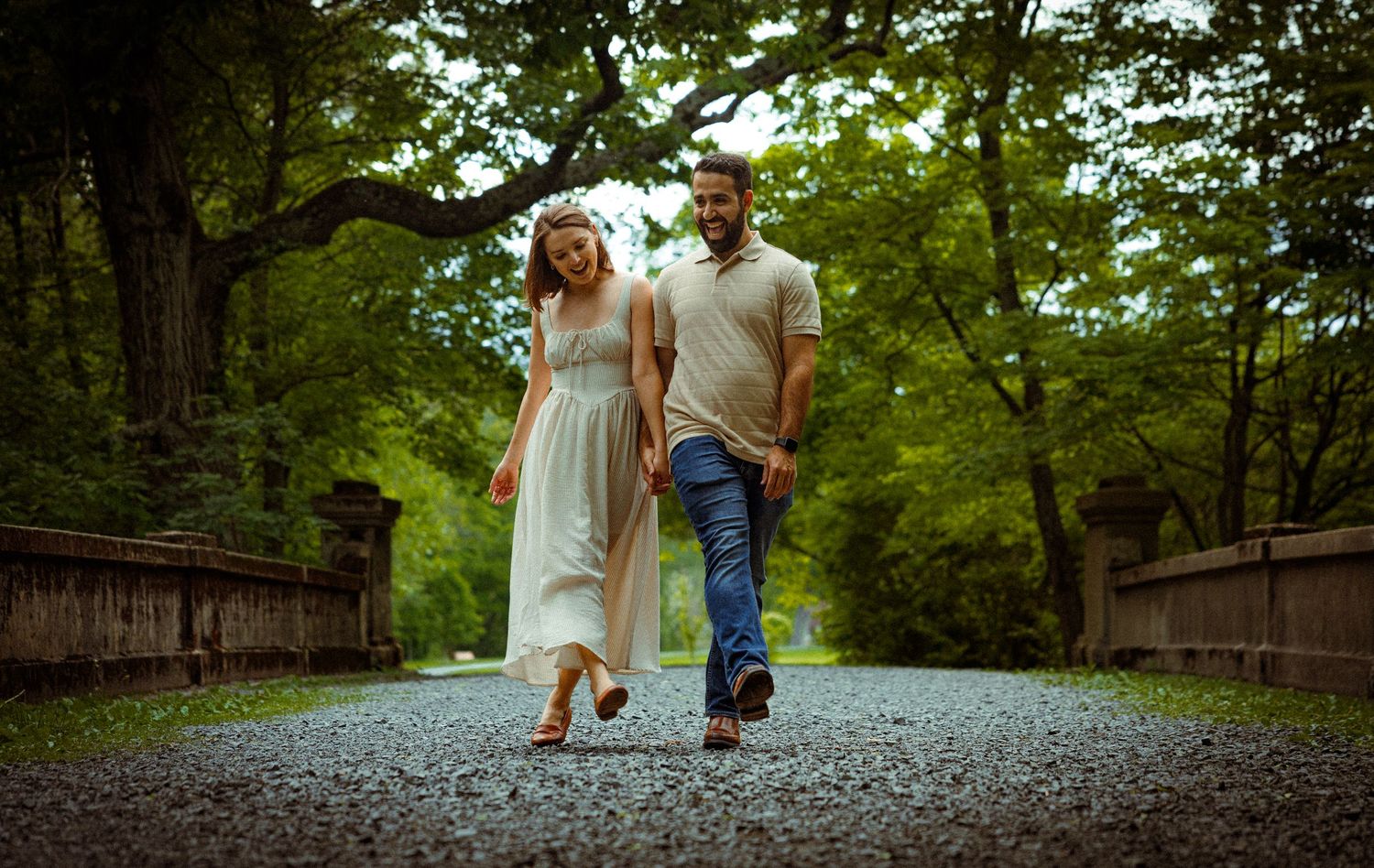 A couple shares tender moments while walking along a gravel path surrounded by trees.