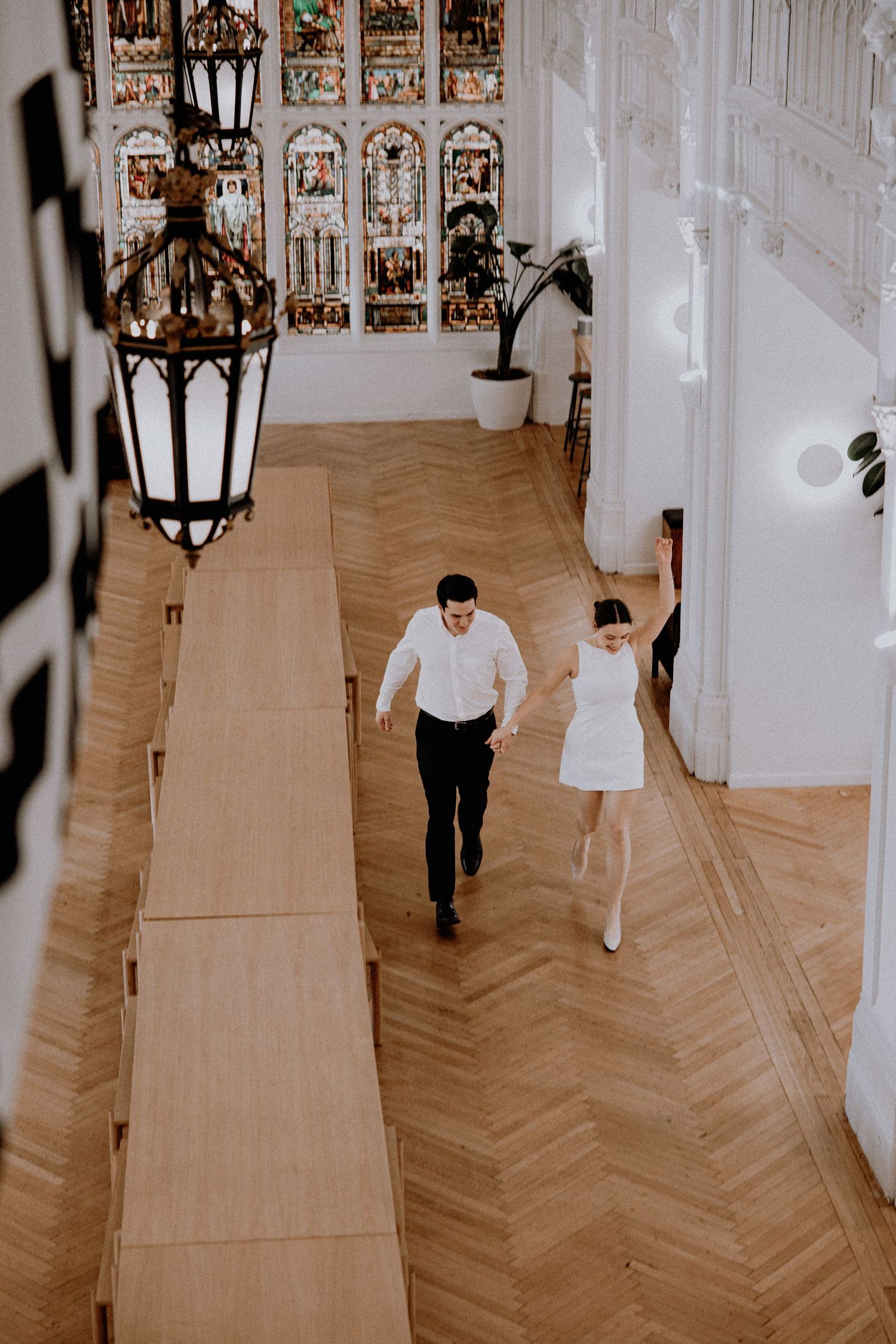 Couple walking through an ornate hallway with herringbone floors and decorative lanterns.