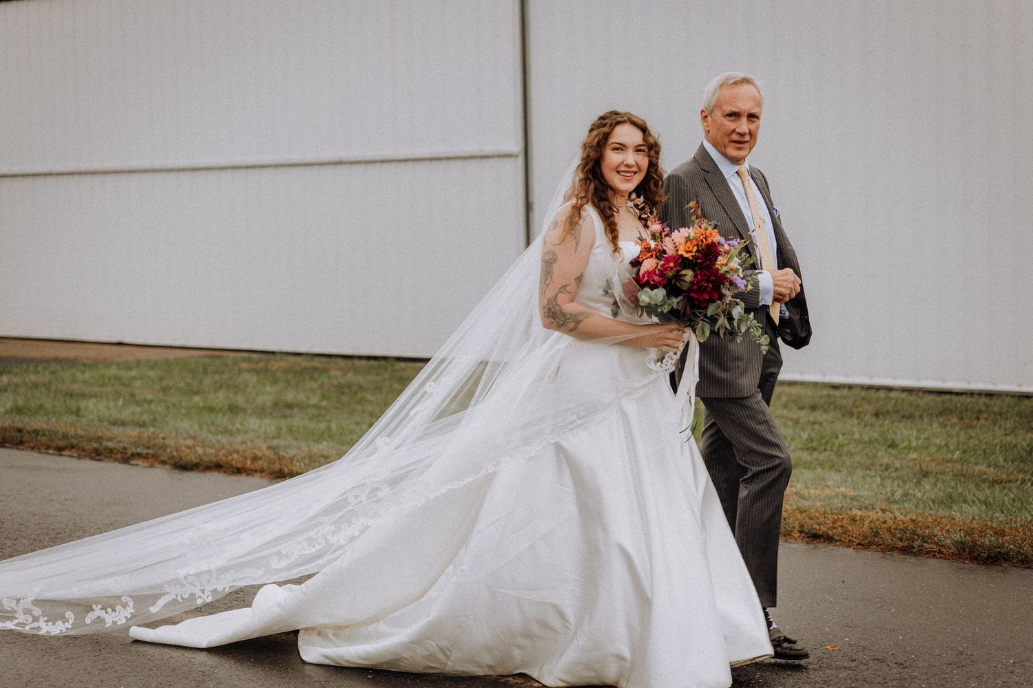 Bride in flowing white gown with long train walks alongside an escort.