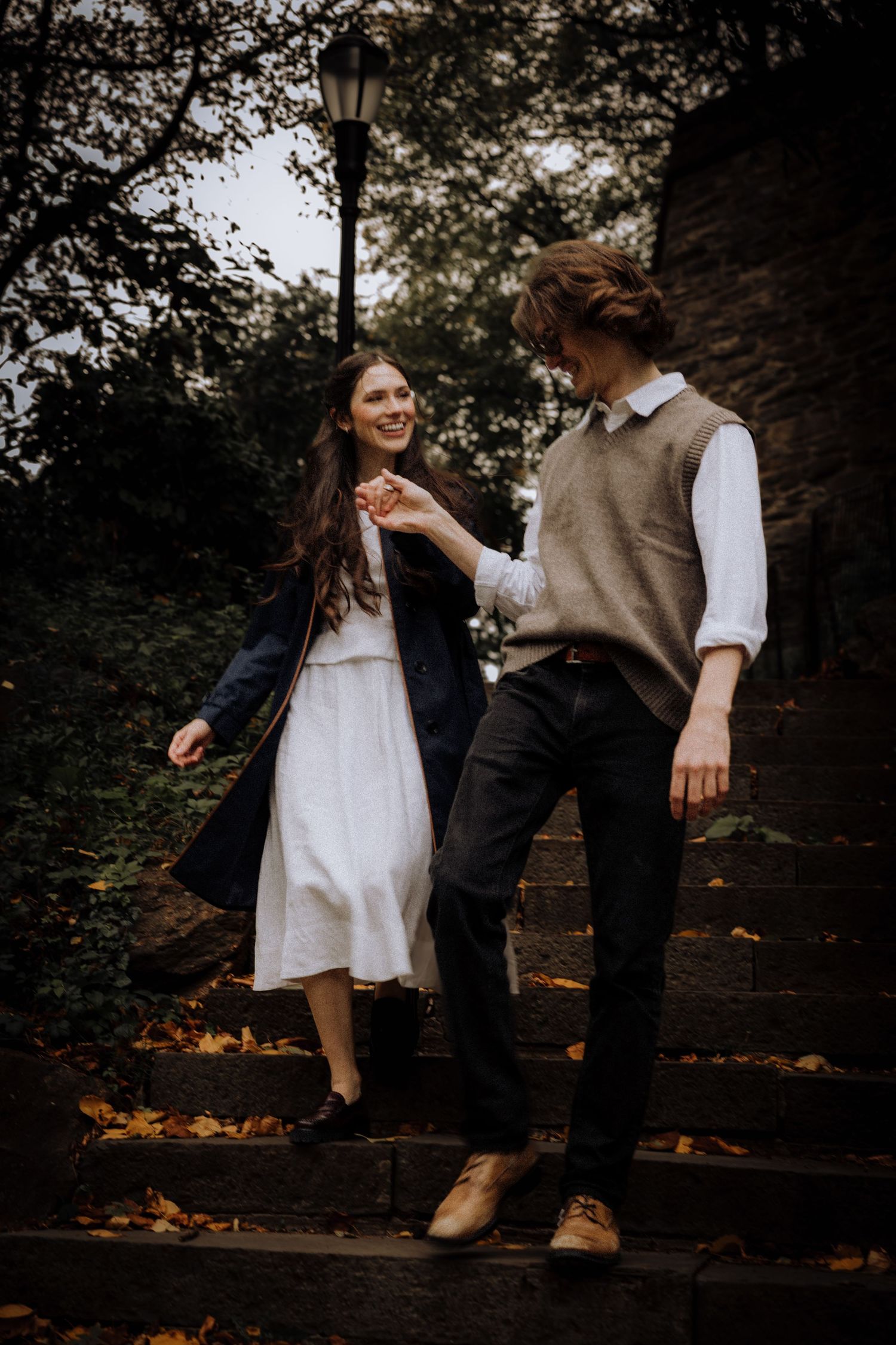 A couple shares playful moments on stone steps surrounded by autumn foliage.