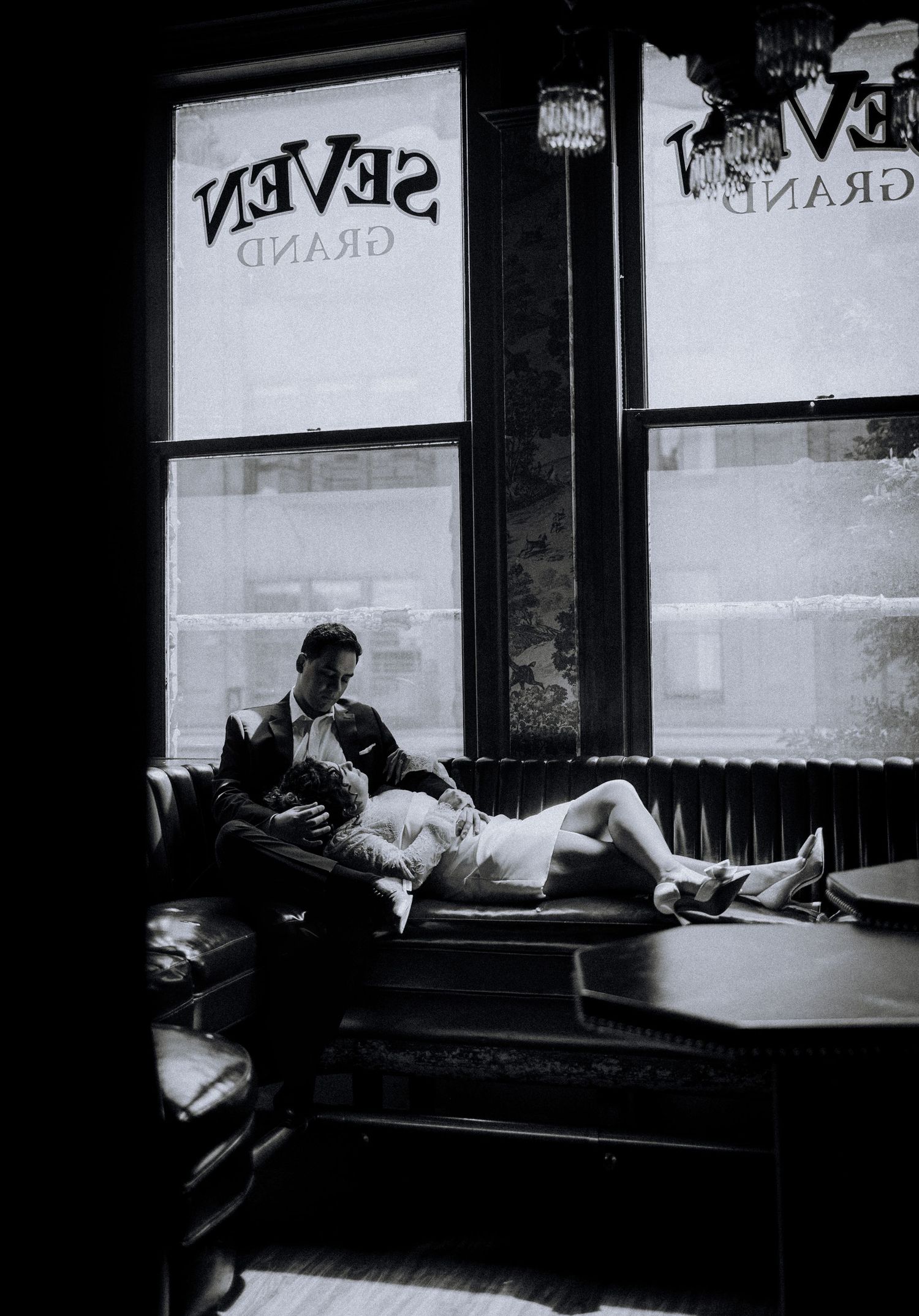 Black and white photo of a couple relaxing on a leather sofa inside Seven Grand bar, Los Angeles.