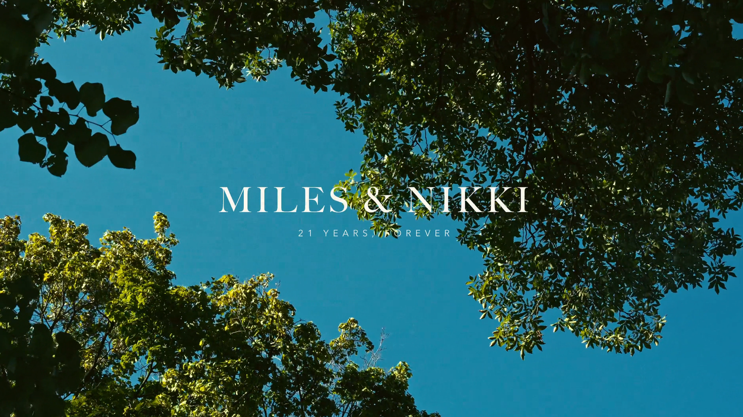 Miles & Nikki wedding title card with text overlay on a blue sky framed by lush green tree canopy.