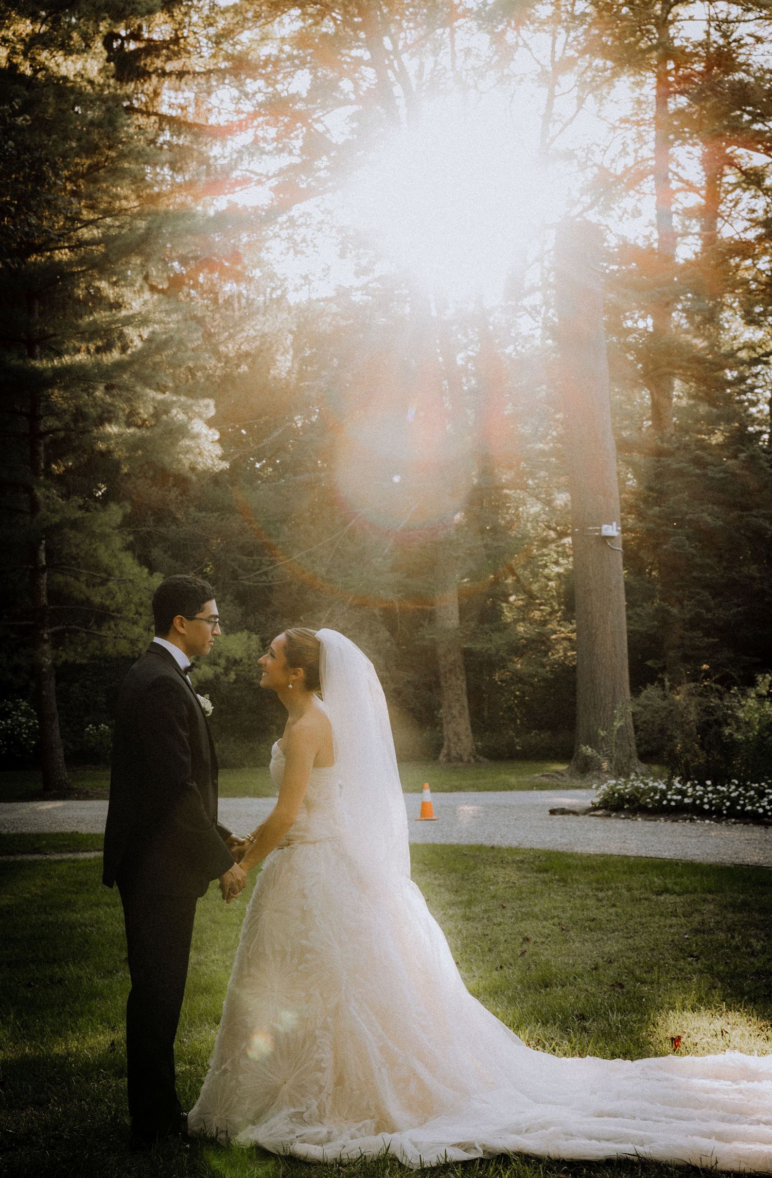 A bride and groom share a romantic moment in a sunlit forest garden, with golden rays streaming through tall trees.