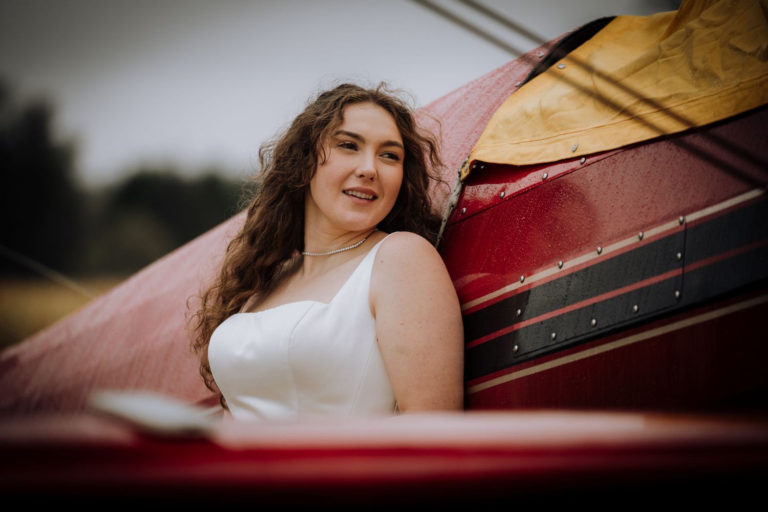 A bride in a white dress poses next to a vintage red airplane.