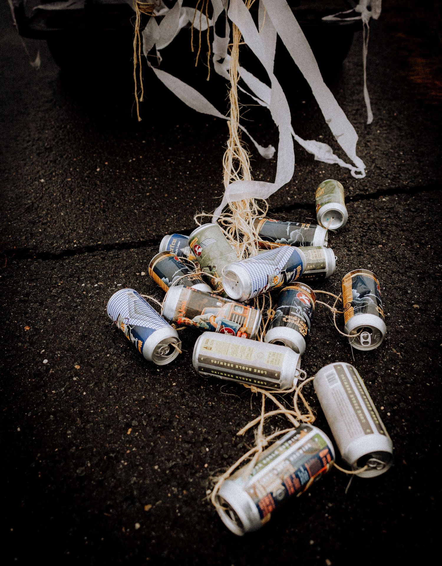 Empty beer cans tied together with string lying on dark ground.