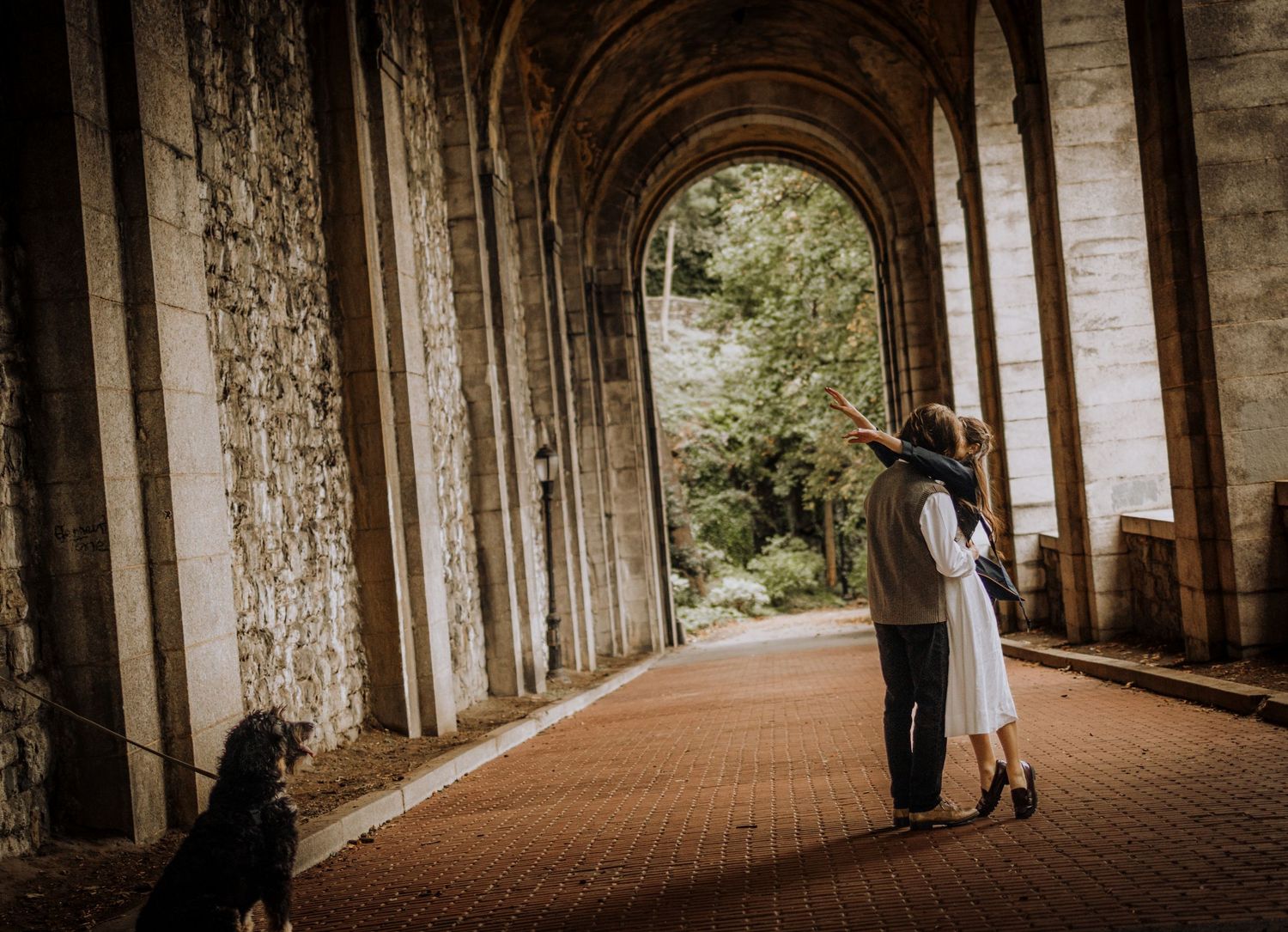 A romantic moment captured in an arched stone colonnade with dramatic lighting.