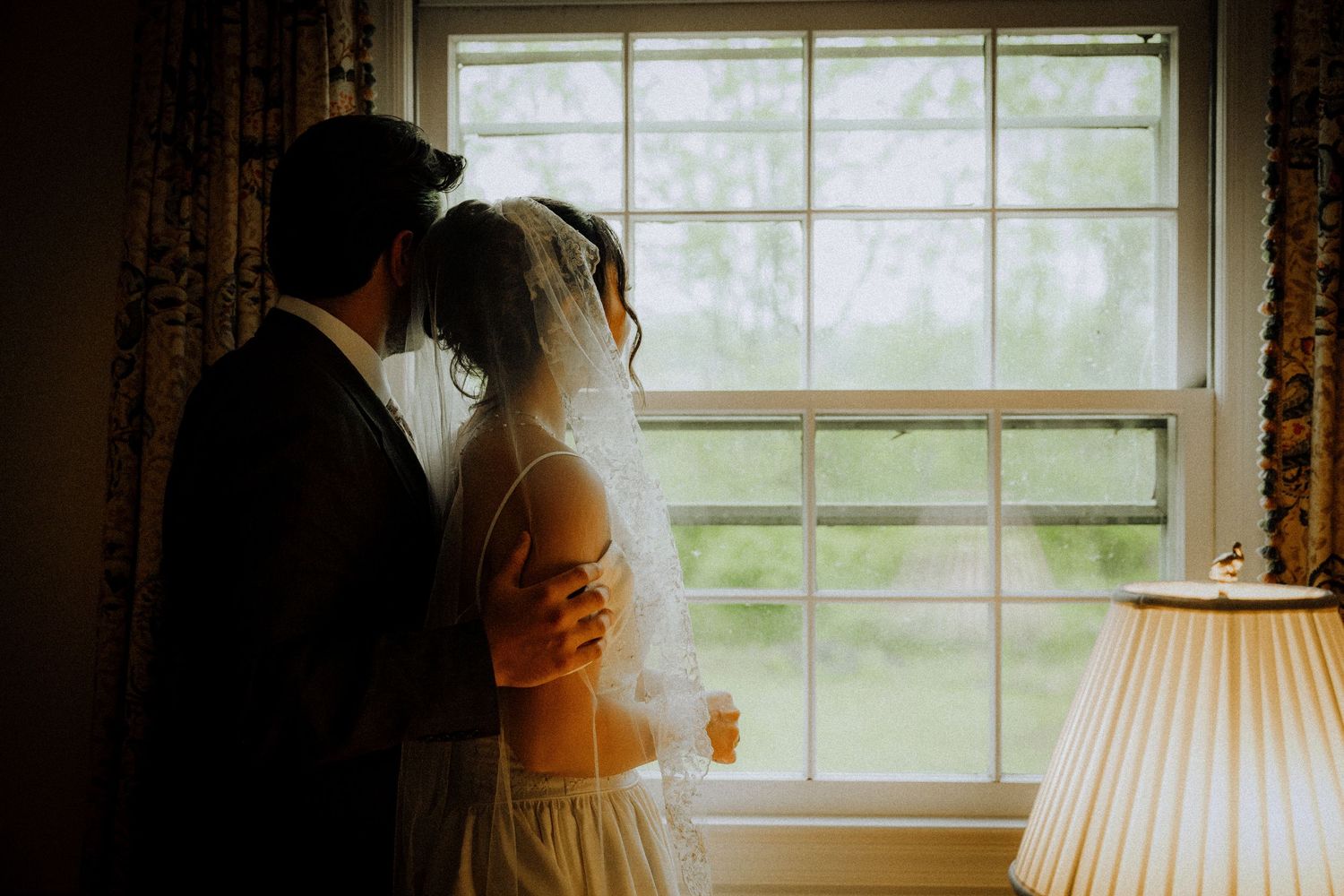 Bride and groom silhouetted against a bright window, sharing an intimate embrace on their wedding day.