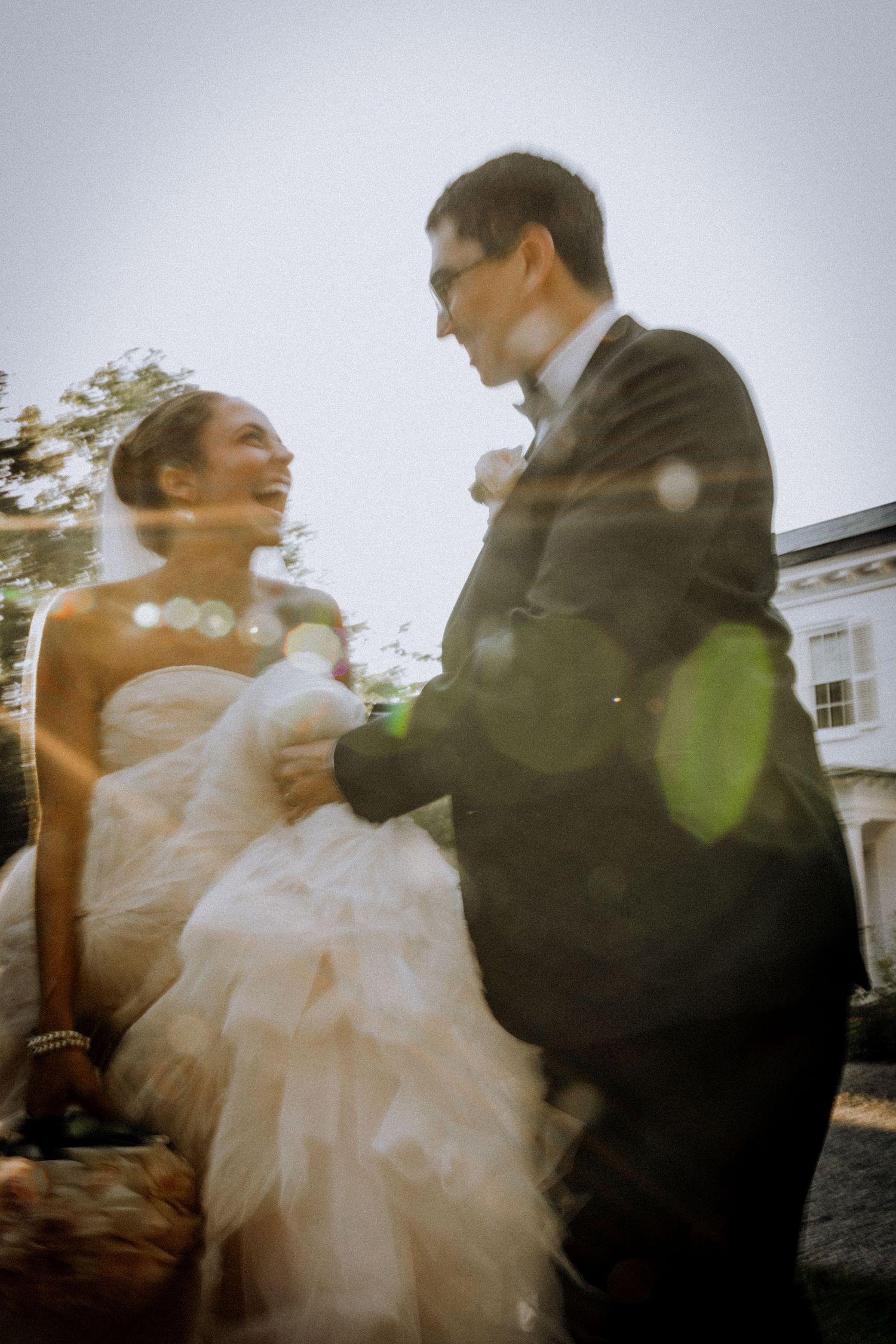 A bride and groom share a joyful moment outdoors, with soft lens flare adding a dreamy quality to their wedding day.