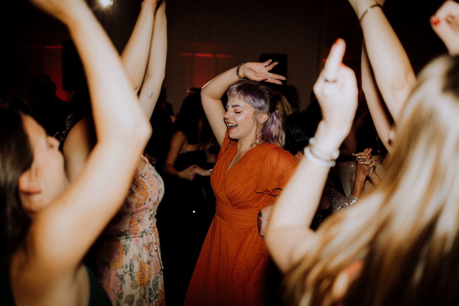 Silhouettes of people dancing with raised arms at a lively wedding reception.
