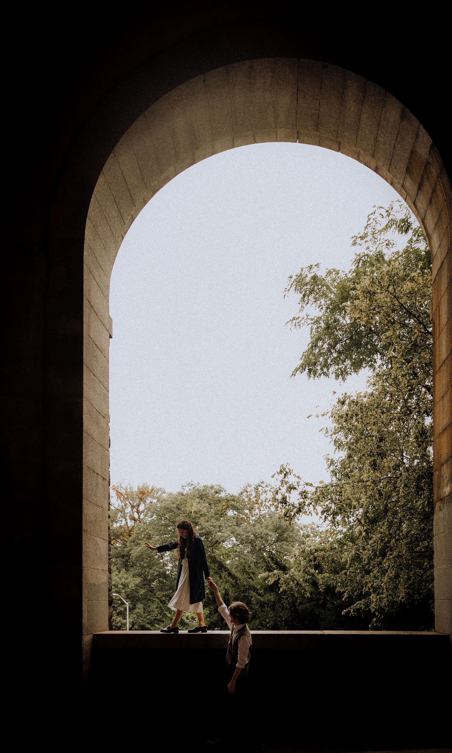 A silhouetted scene through a stone archway overlooking trees in natural light.