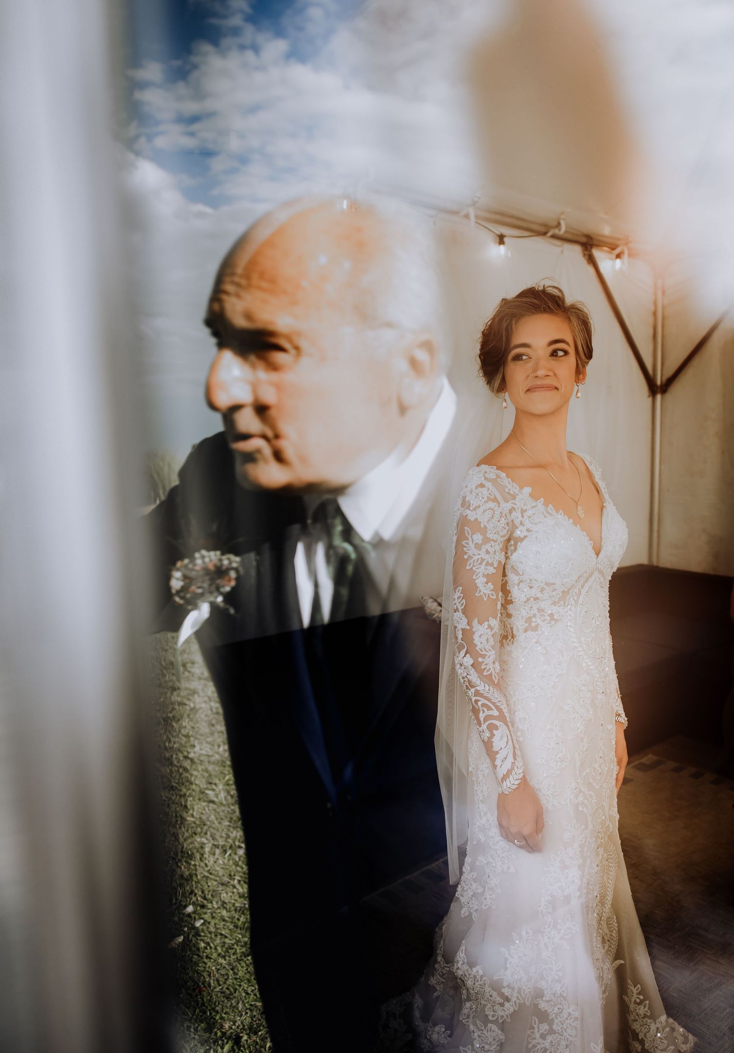 Artistic double exposure wedding portrait showing bride in lace dress with older man in foreground.