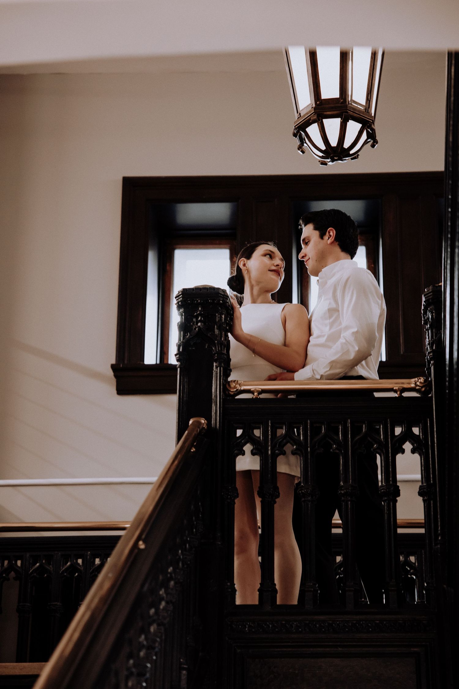 Romantic moment shared on vintage staircase with ornate black railings and pendant lighting.
