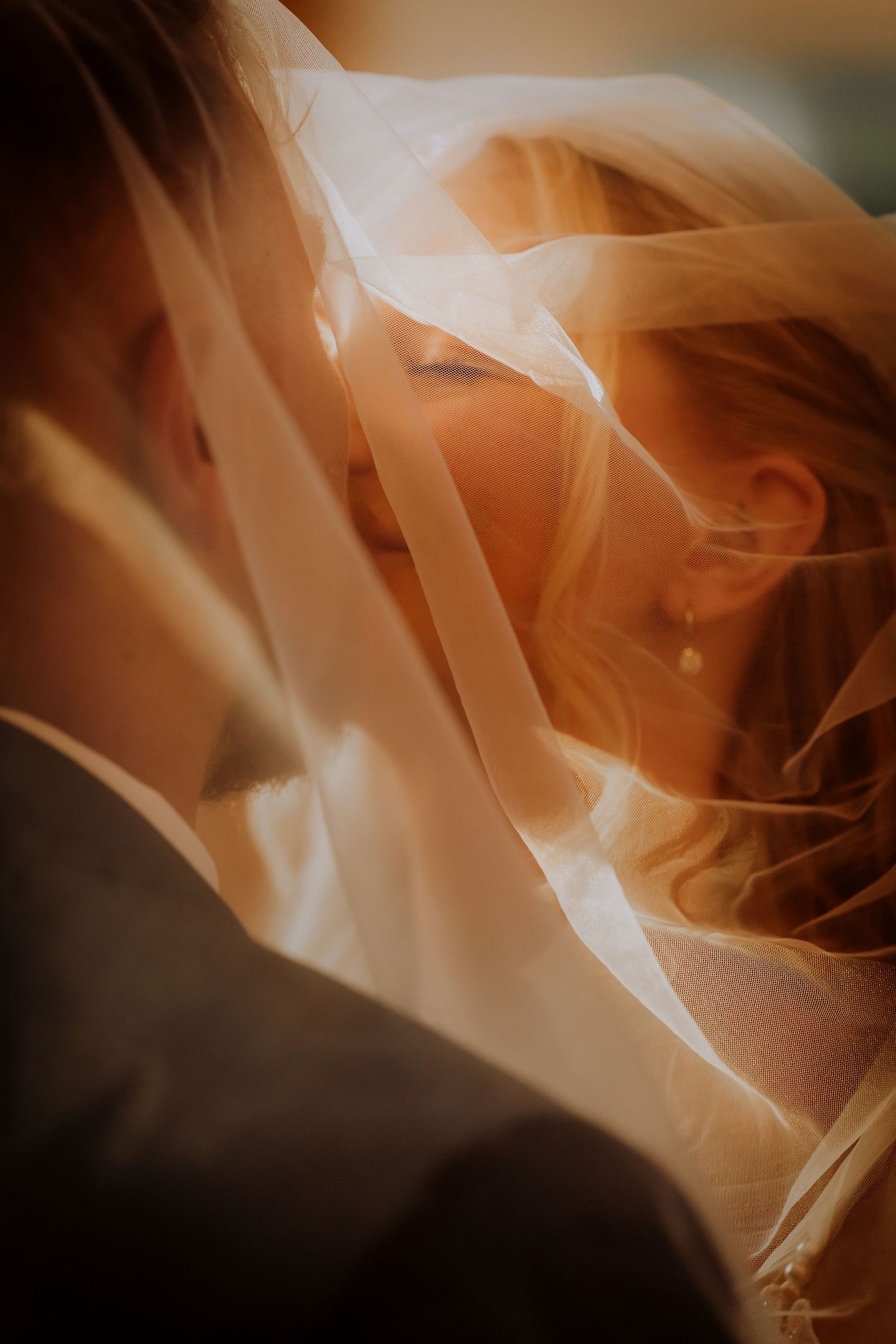 Romantic close-up through delicate white wedding veil with soft golden lighting.Editorial and Cinematic Wedding photos