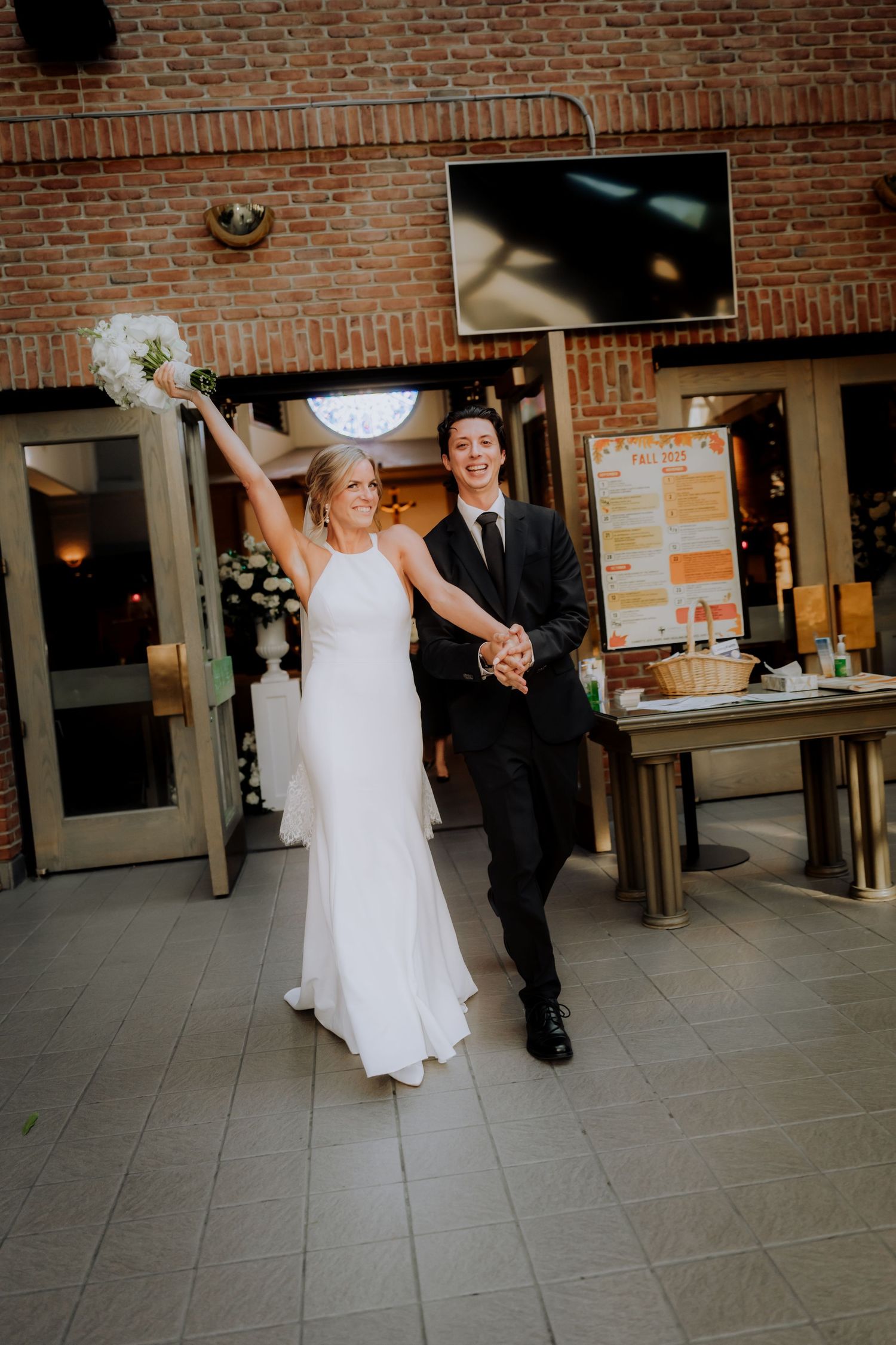 A celebratory moment as newlyweds make their entrance into a brick-walled reception venue.Editorial and Cinematic Wedding photos