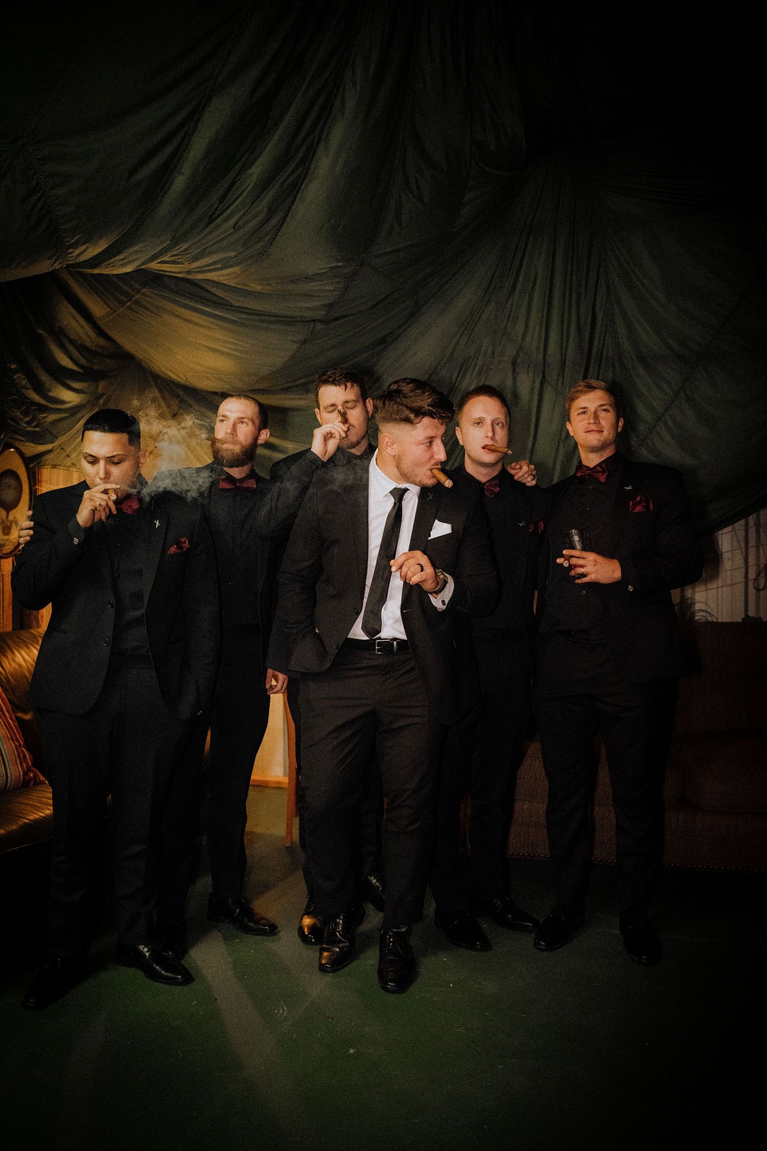 Groomsmen in black suits posing dramatically in a low-light setting with dark backdrop.